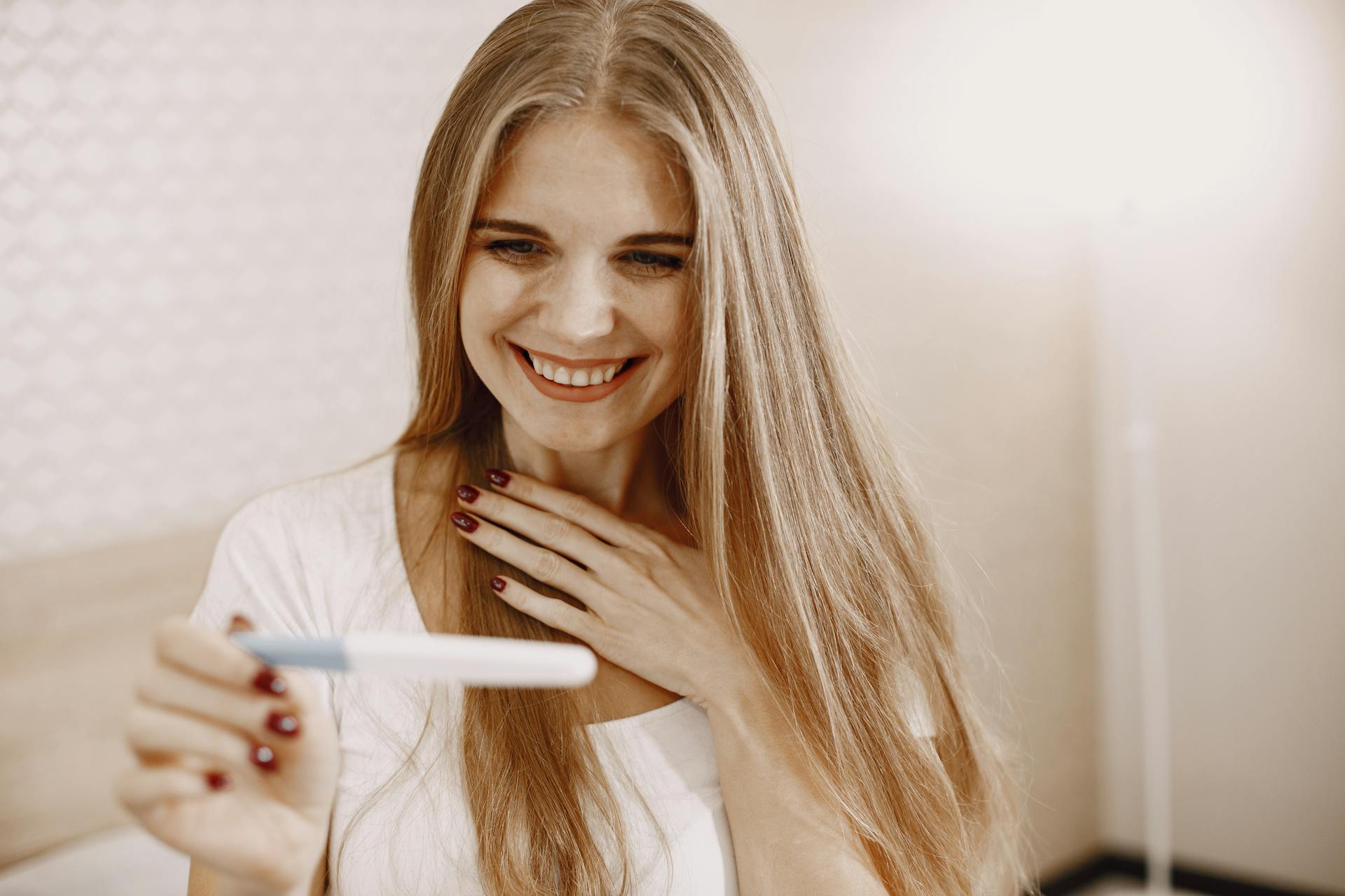 A delighted woman holding a pregnancy test kit | Source: Pexels