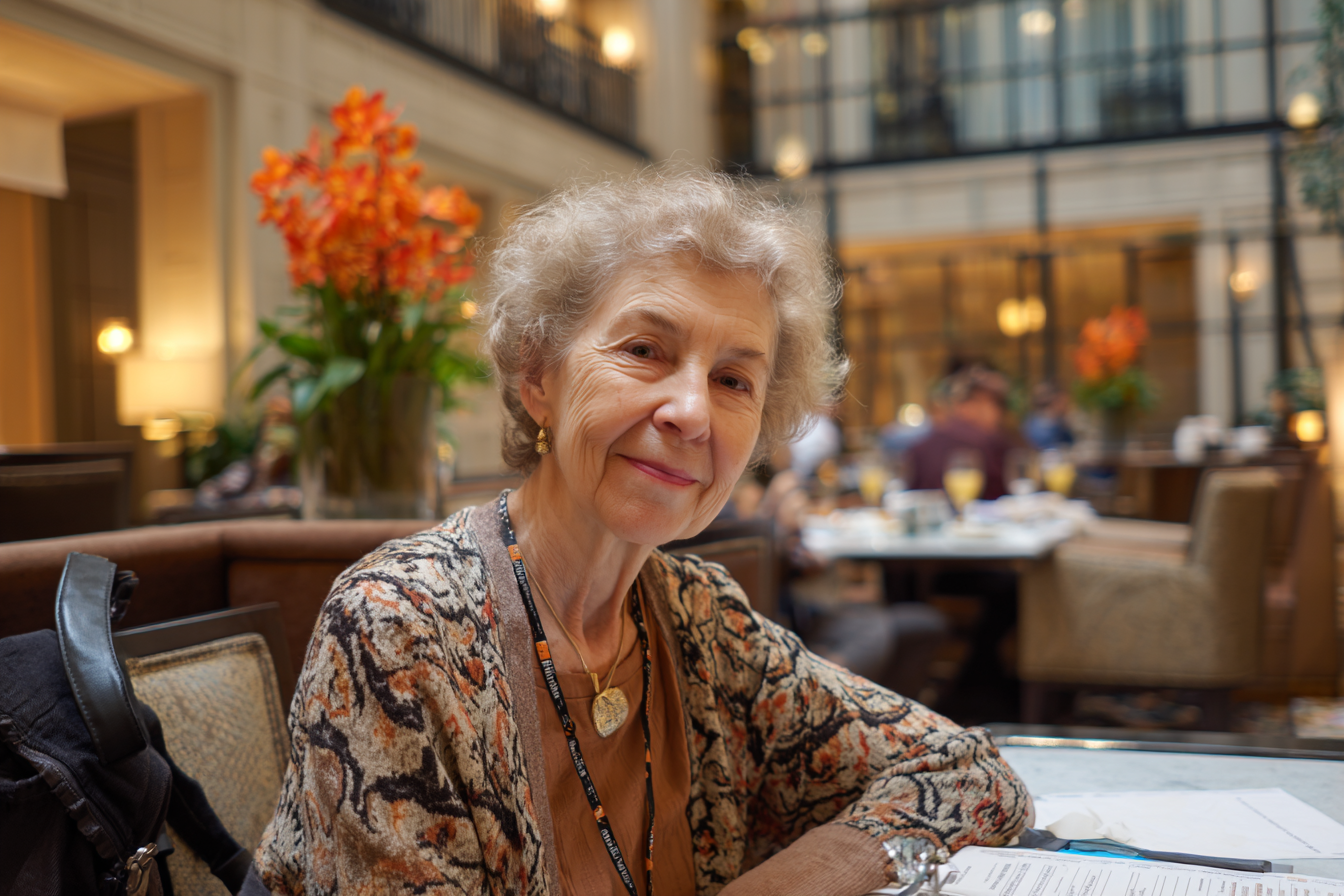 A woman seated at a table in a hotel restaurant smiling at someone | Source: Midjourney