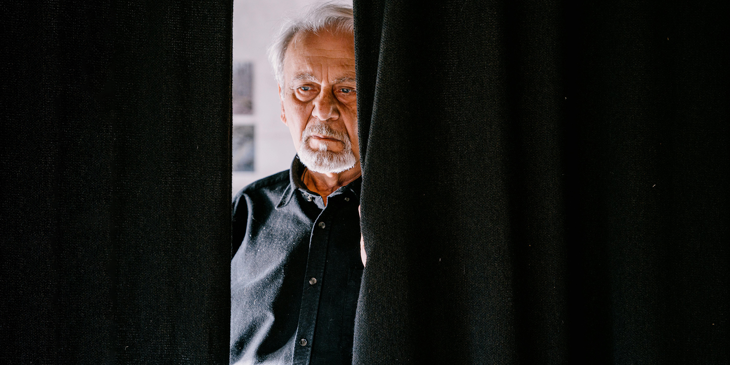 Sad man standing behind the curtain | Source: Pexels