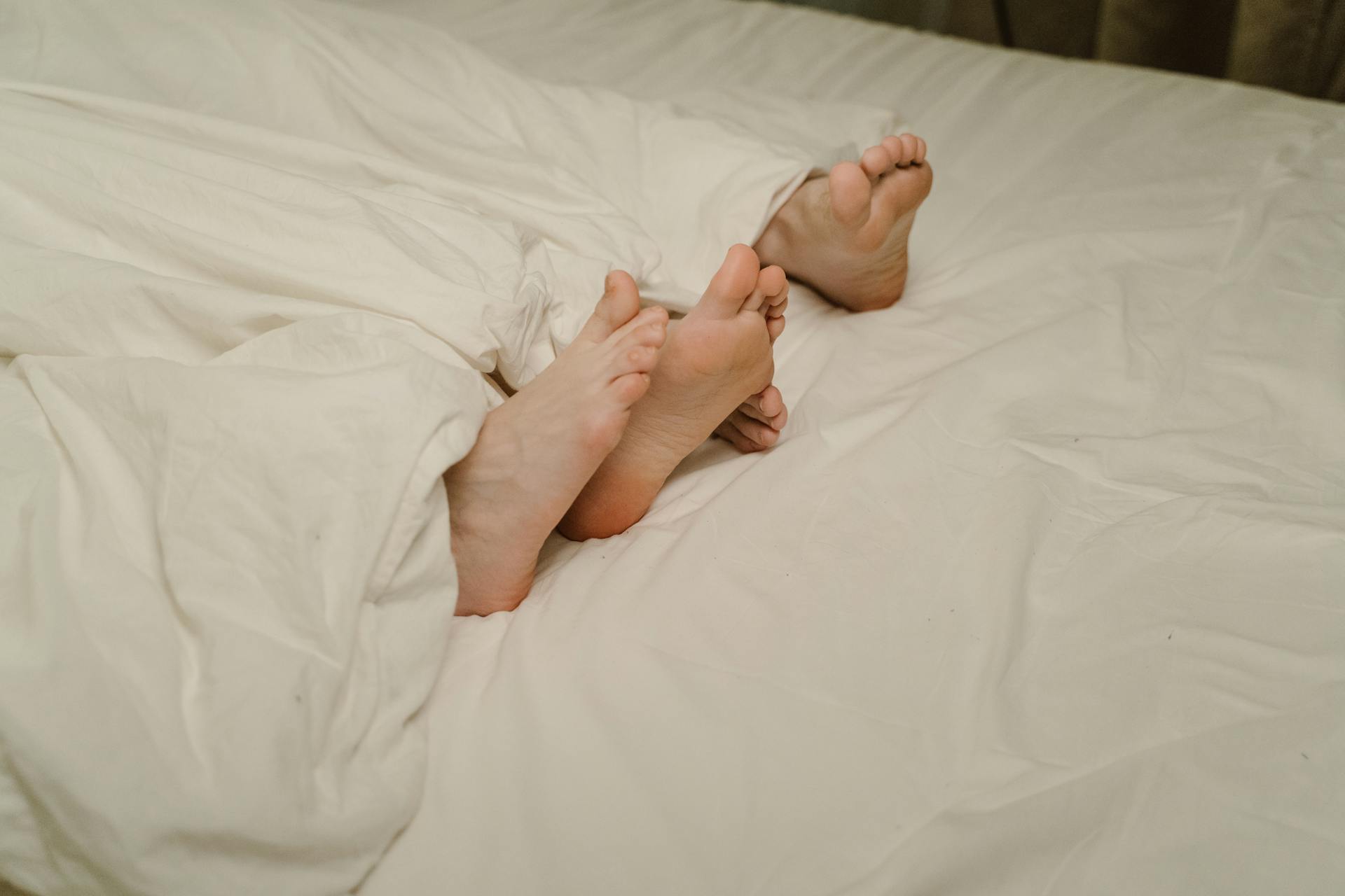 People's feet protruding from bedcovers | Source: Pexels