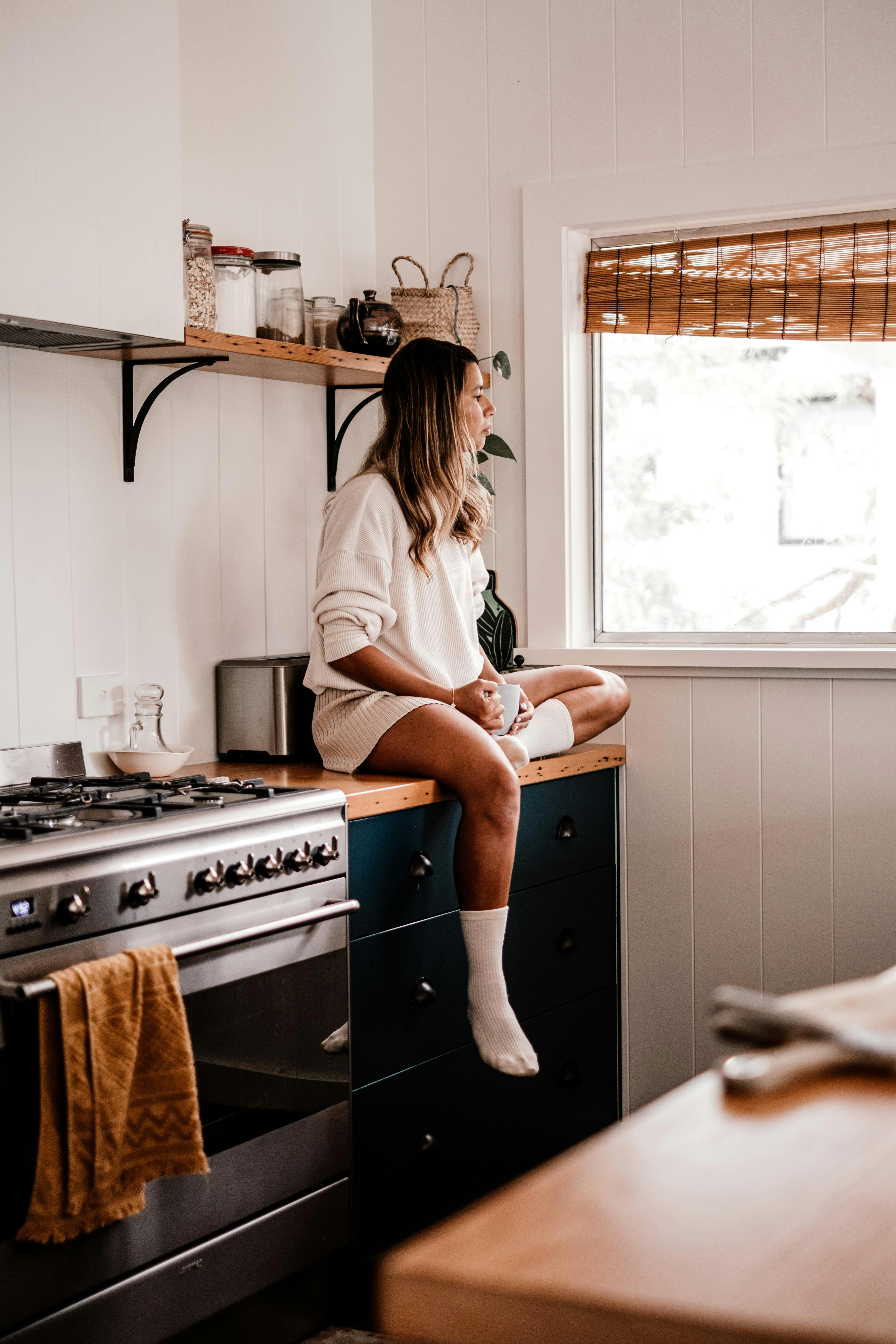 Woman sitting on a kitchen counter looking outside | Source: Pexels