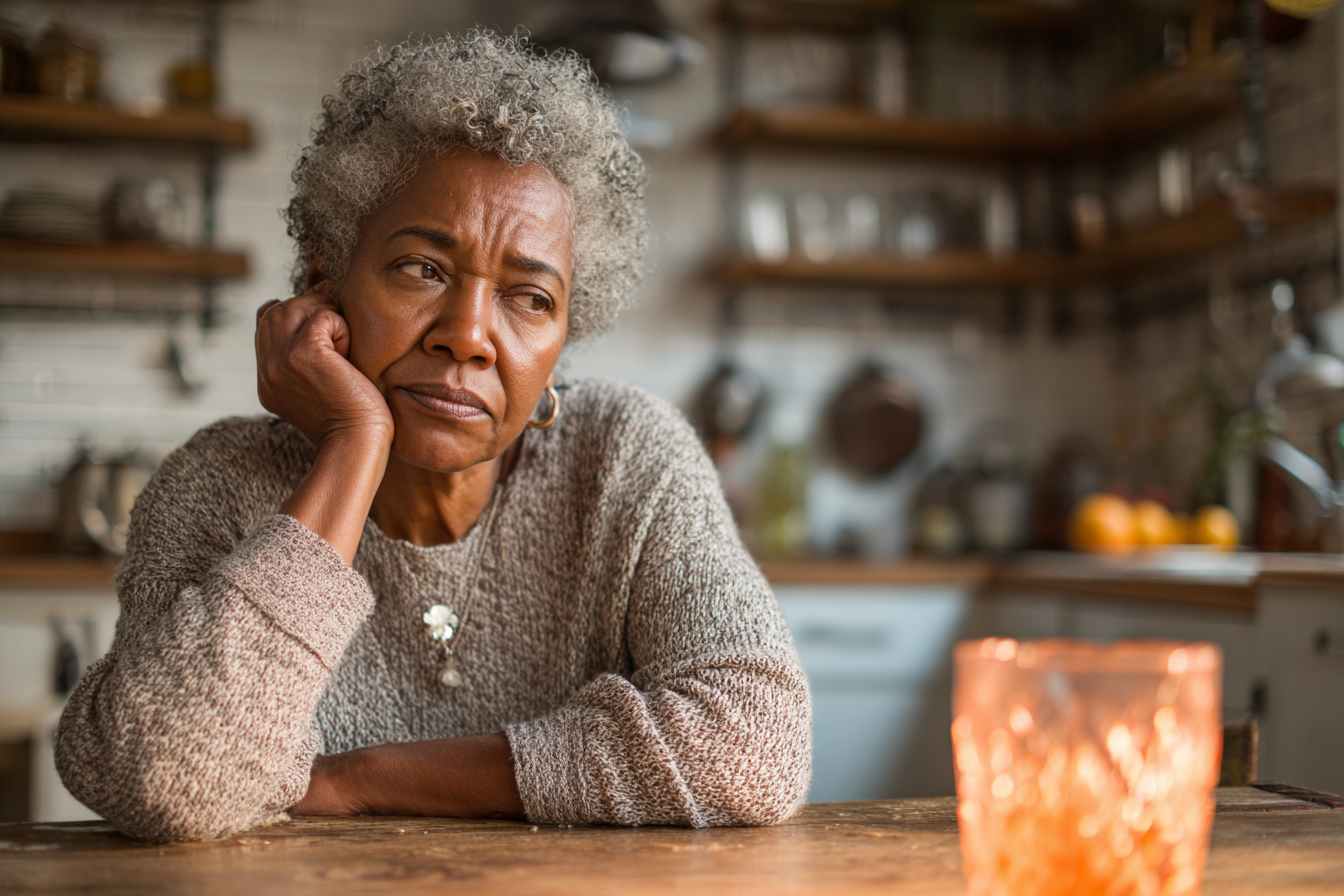 A sad-looking woman seated at a kitchen table | Source: Midjourney
