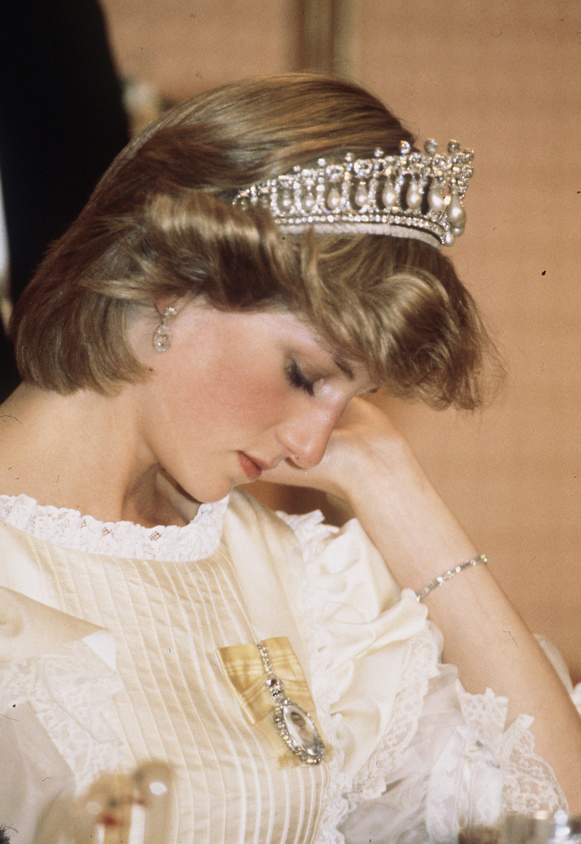 Diana, Princess of Wales, wearing a cream satin dress by Gina Fratini with the Queen Mary Cambridge Lover's Knot Tiara and diamond earrings, looks tired as she attends a banquet on April 29, 1983 in Auckland, New Zealand. | Source: Getty Images