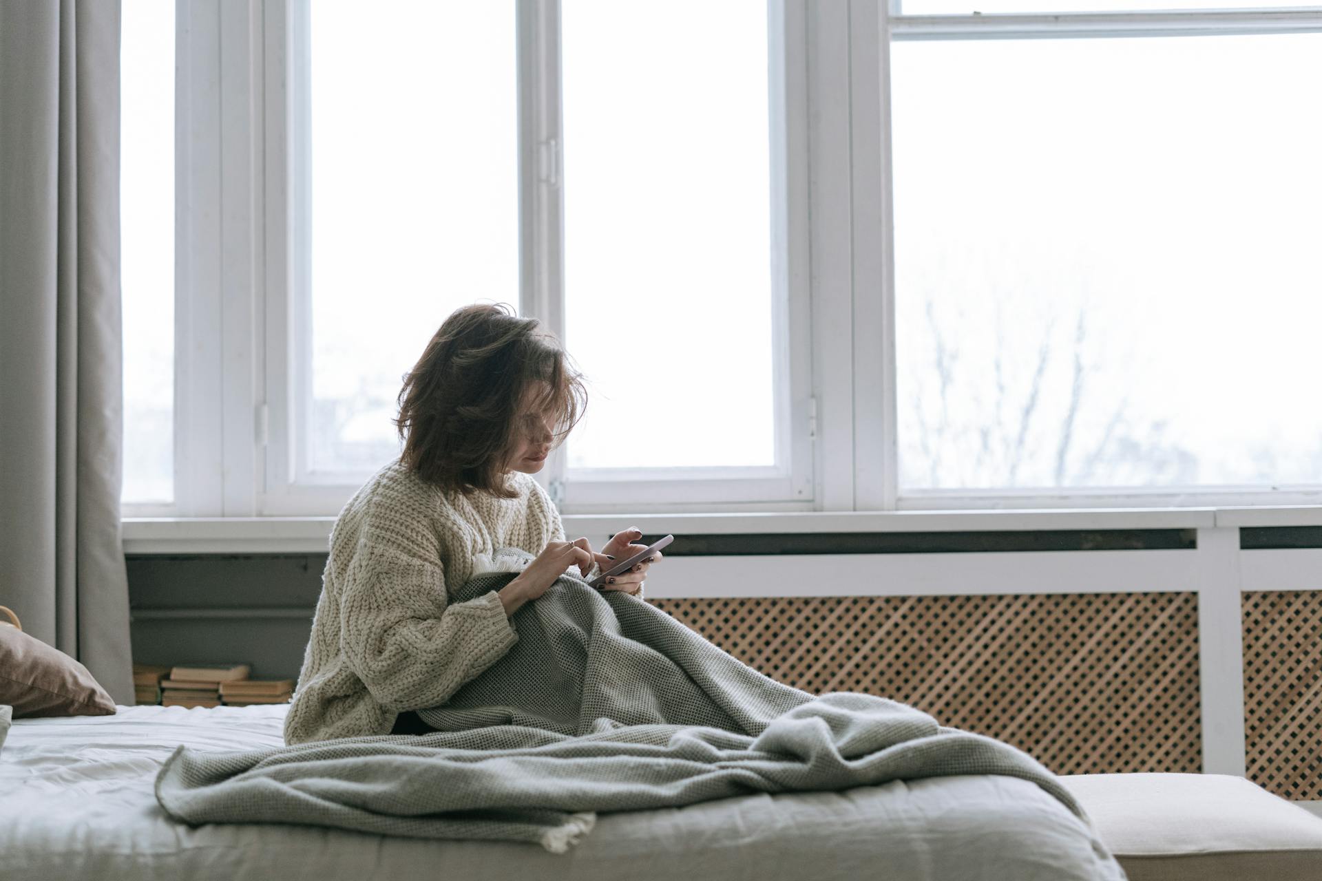 A young woman using her phone while sitting in bed | Source: Pexels