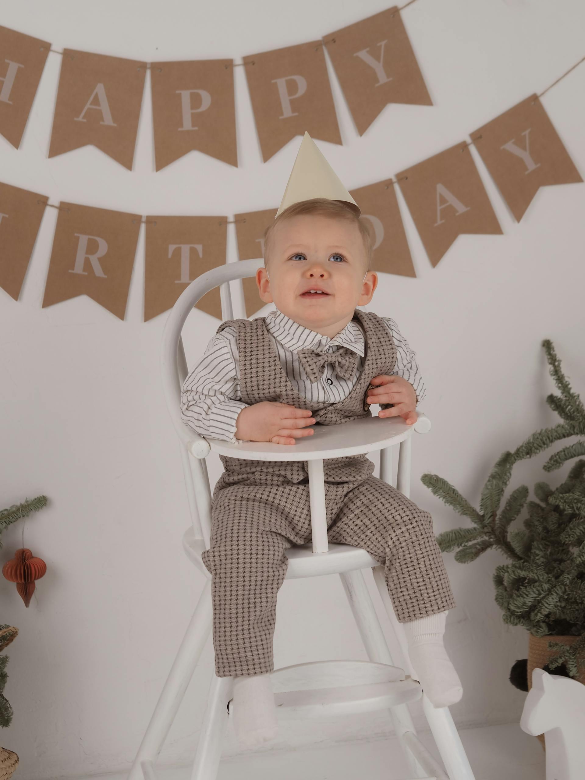 A little boy wearing a party hat and sitting on a white high chair on his birthday | Source: Pexels