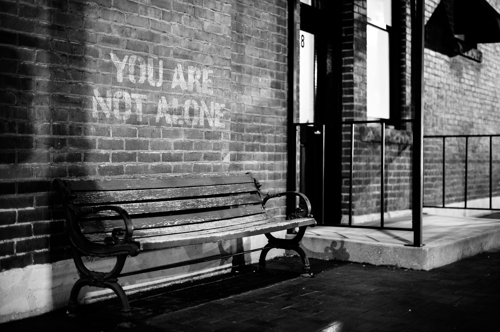 A bench near a brick wall with the inscription "You are not alone" | Source: Pexels