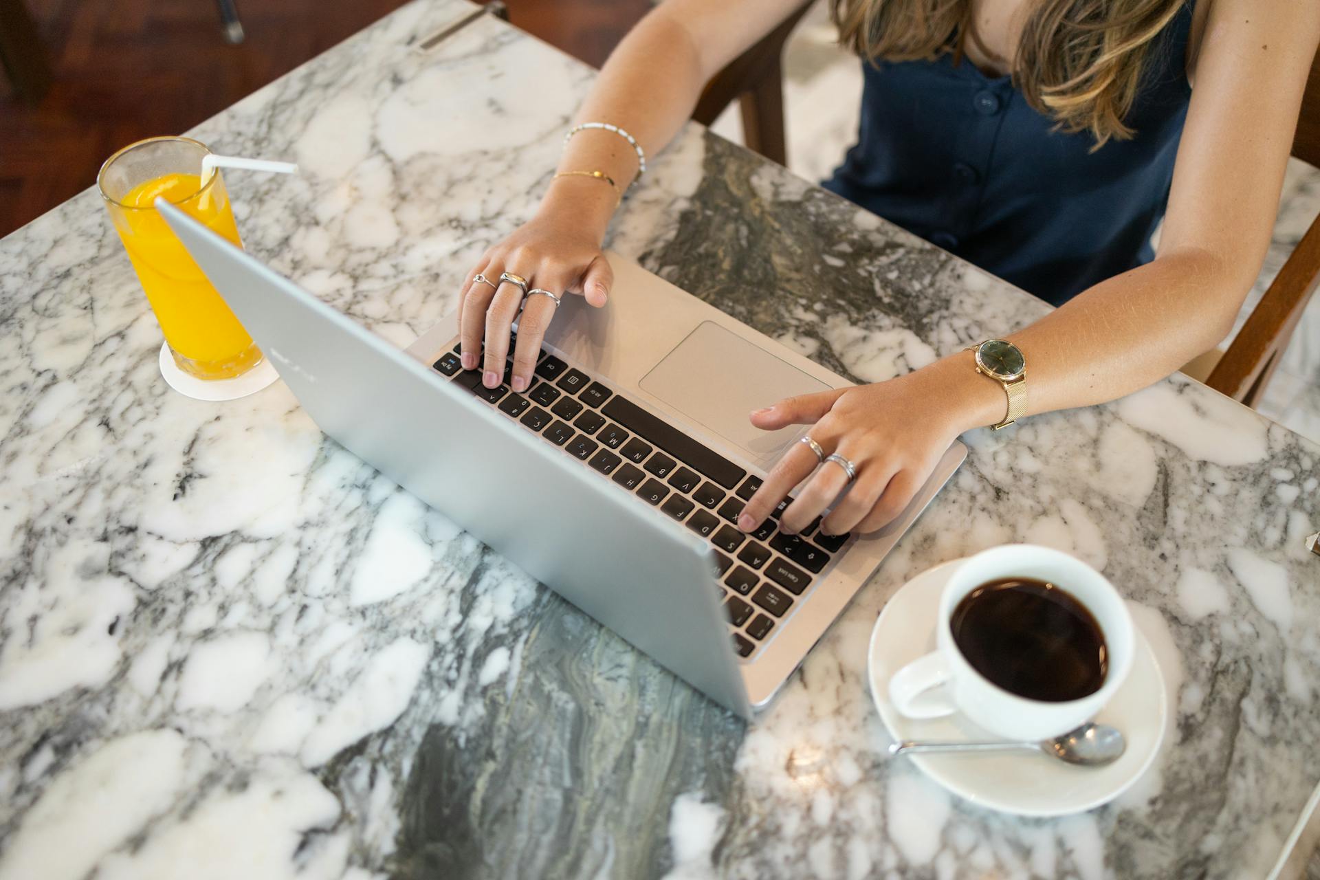A woman working on her laptop with a cup of coffee and juice lying on the table in front of her | Source: Pexels