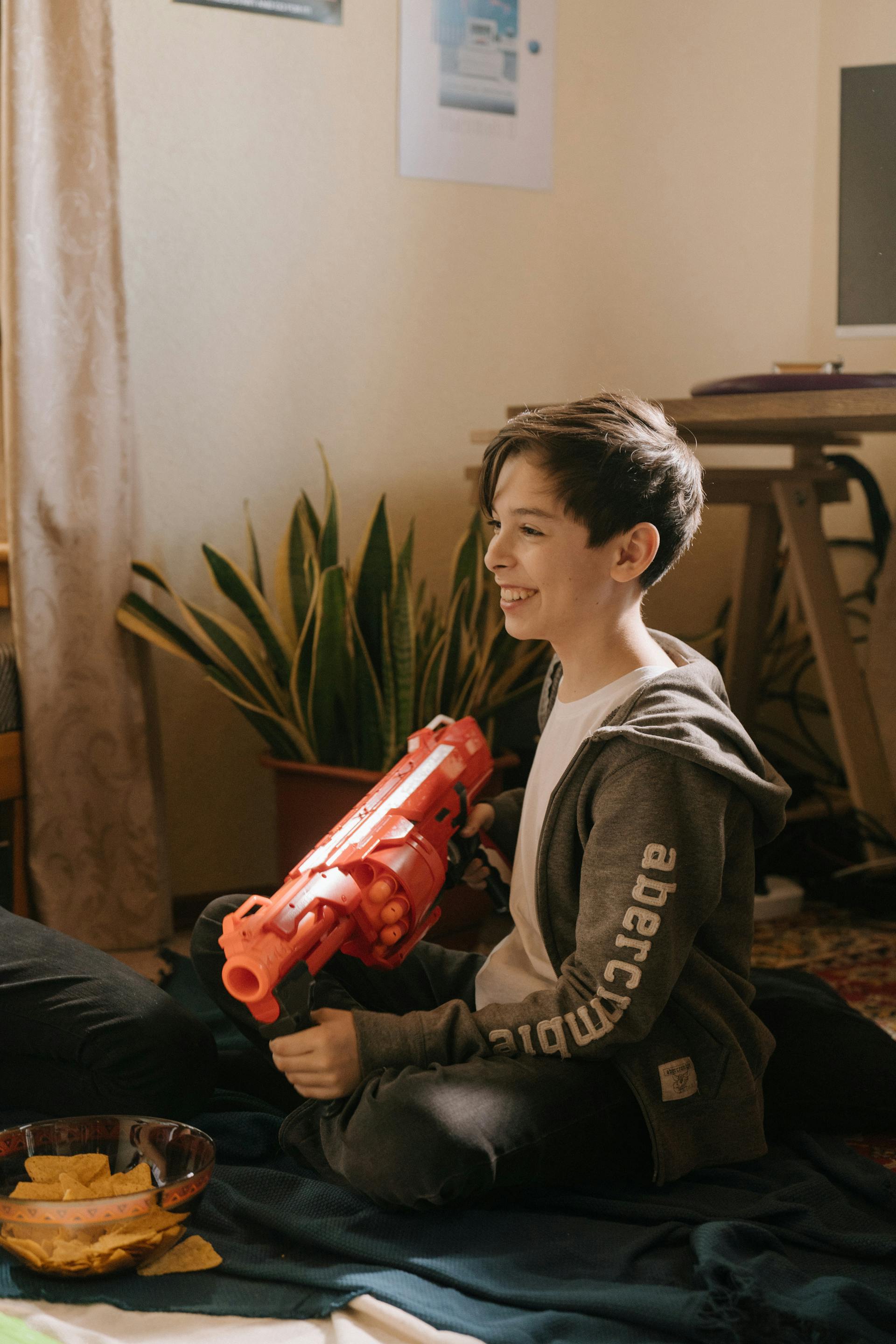 A young boy holding a red plastic toy gun | Source: Pexels