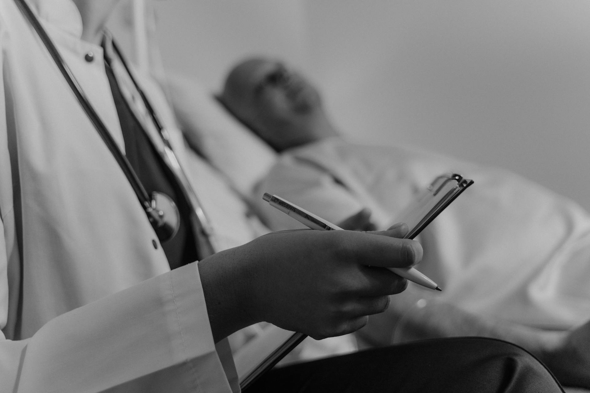 A grayscale photo of a doctor holding a medical chart while standing beside a patient | Source: Pexels