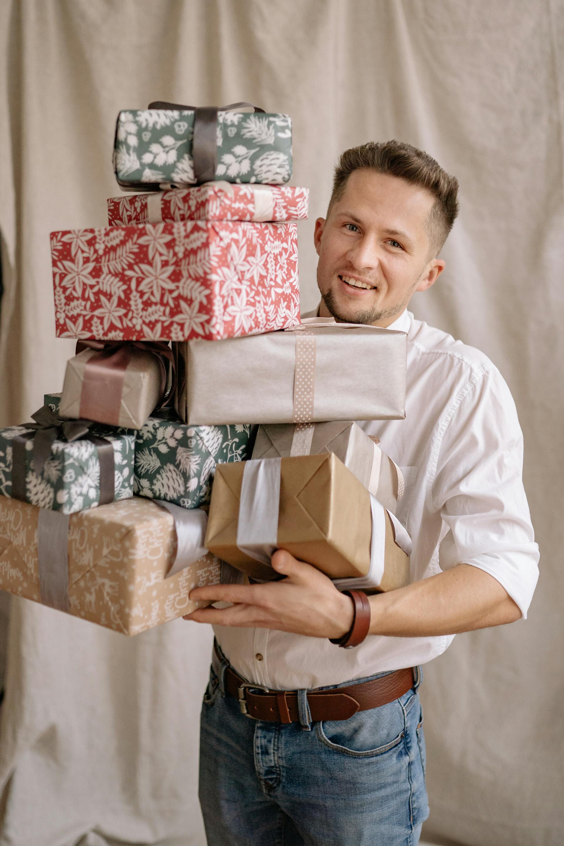 A man in a white shirt and jeans holding a large stack of wrapped presents | Source: Pexels