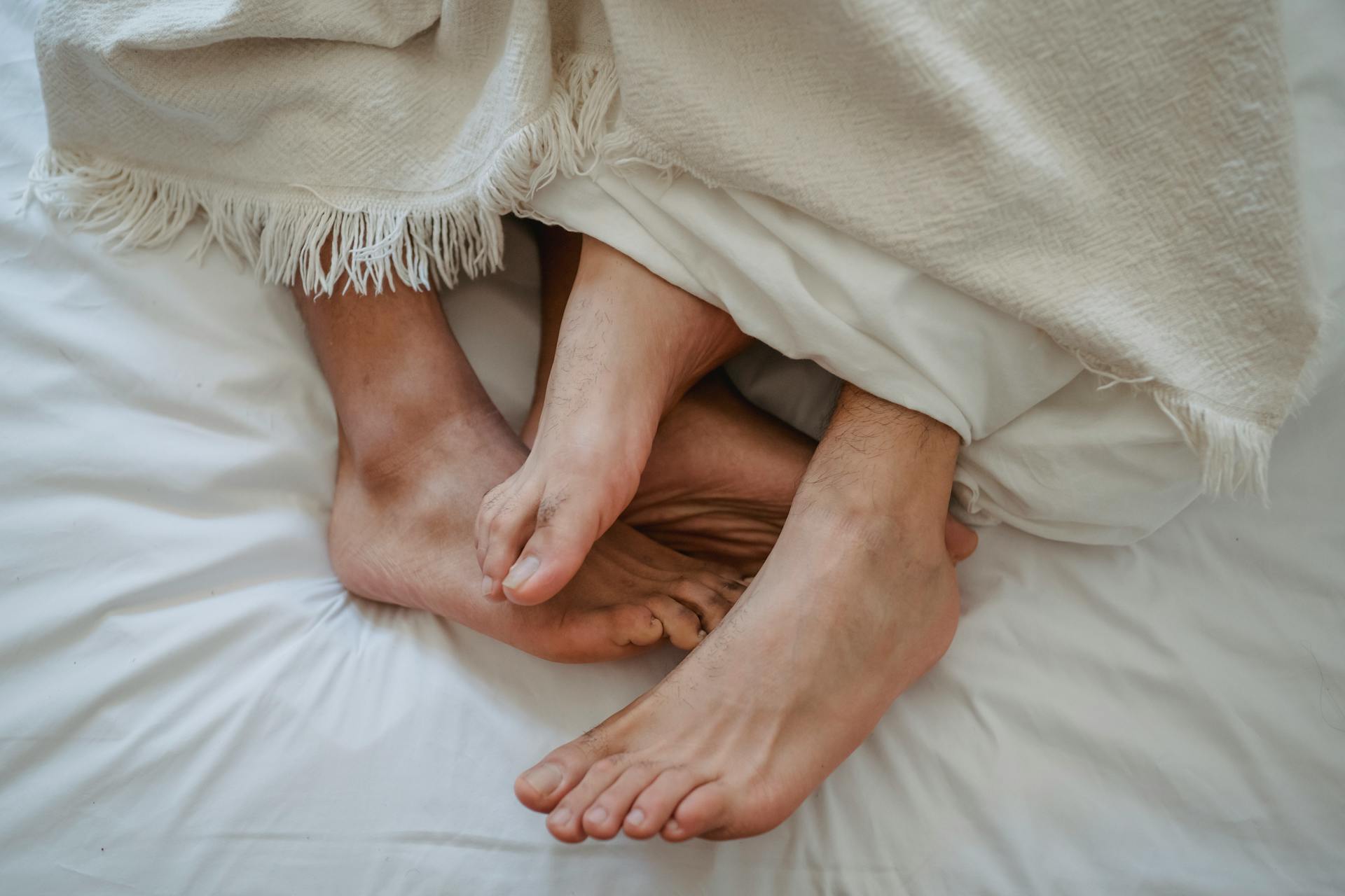 Pés de dois homens entrelaçados na cama | Fonte: Pexels