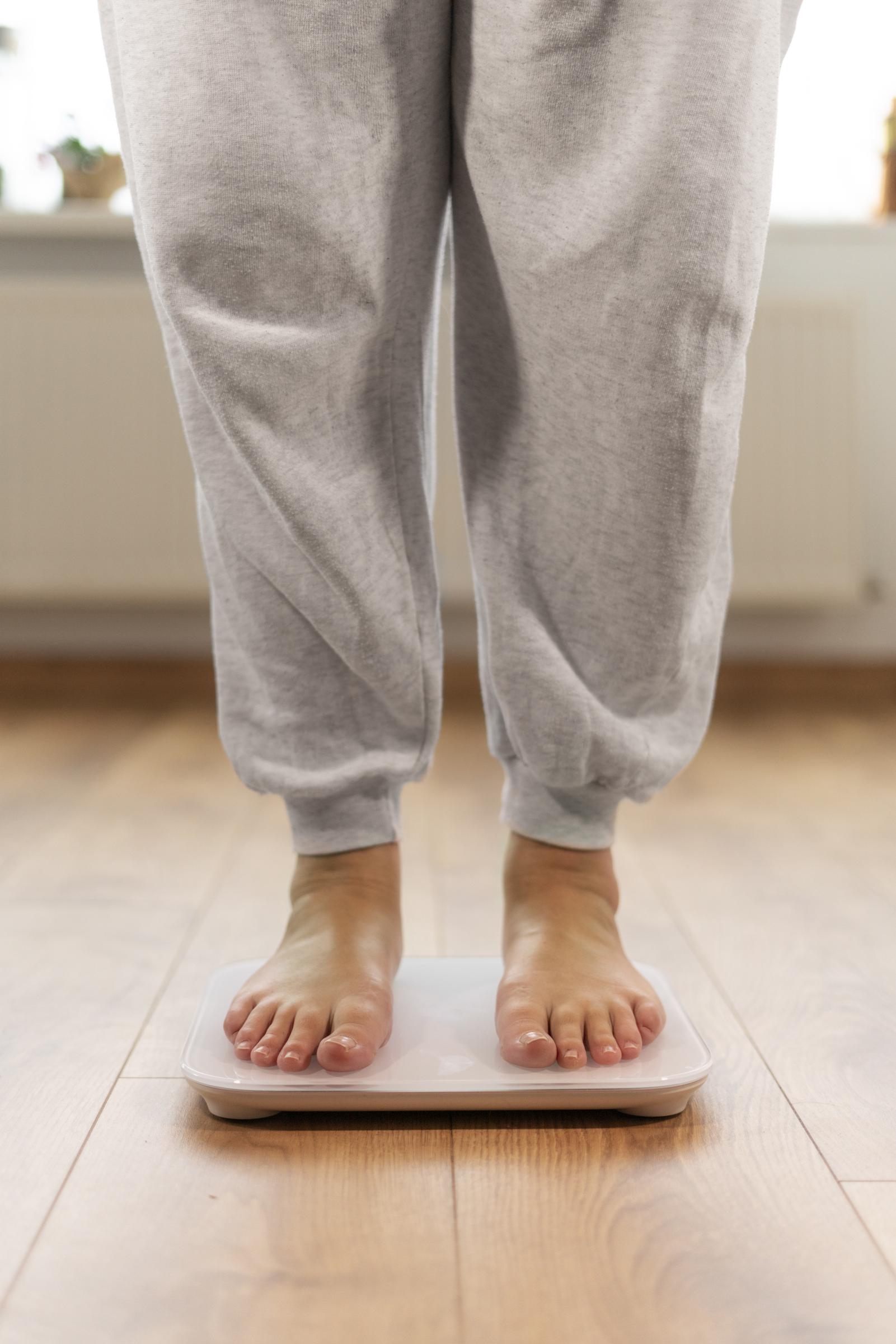 A woman measuring her weight on a weighing scale | Source: Freepik