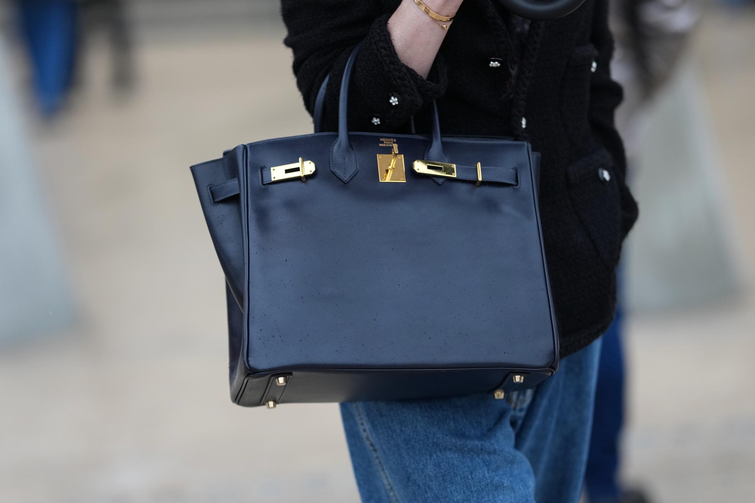 A guest wears a black leather top-handle Birkin bag from Hermes with gold-tone hardware, a black textured jacket with buttoned flap pockets, blue medium-wash denim jeans, outside Chanel, during Paris Fashion Week - Haute Couture - Spring Summer 2026, on January 27, 2026 in Paris, France. | Source: Getty Images