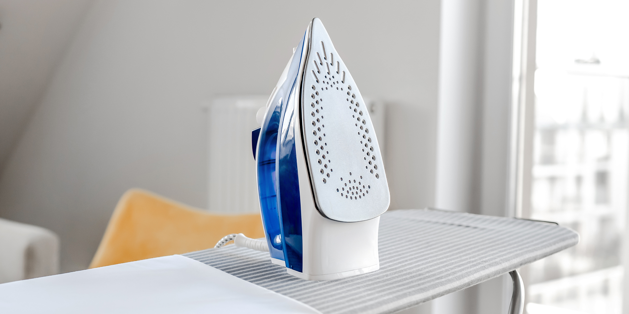 A steam iron kept upright on an ironing board in a bright room | Source: Shutterstock