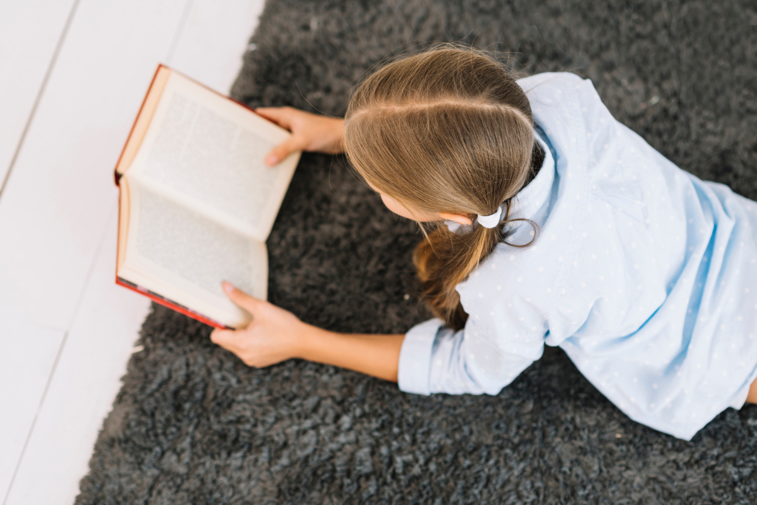 A girl lying on a rug and reading a book | Source: Freepik