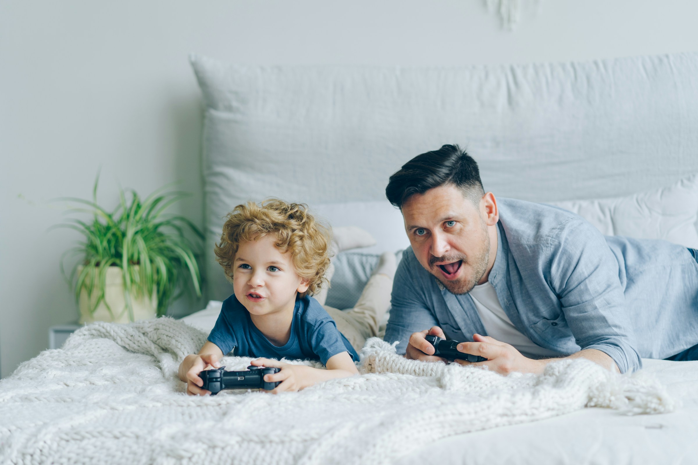 A man and a little boy lying on the bed and playing video game | Source: Unsplash