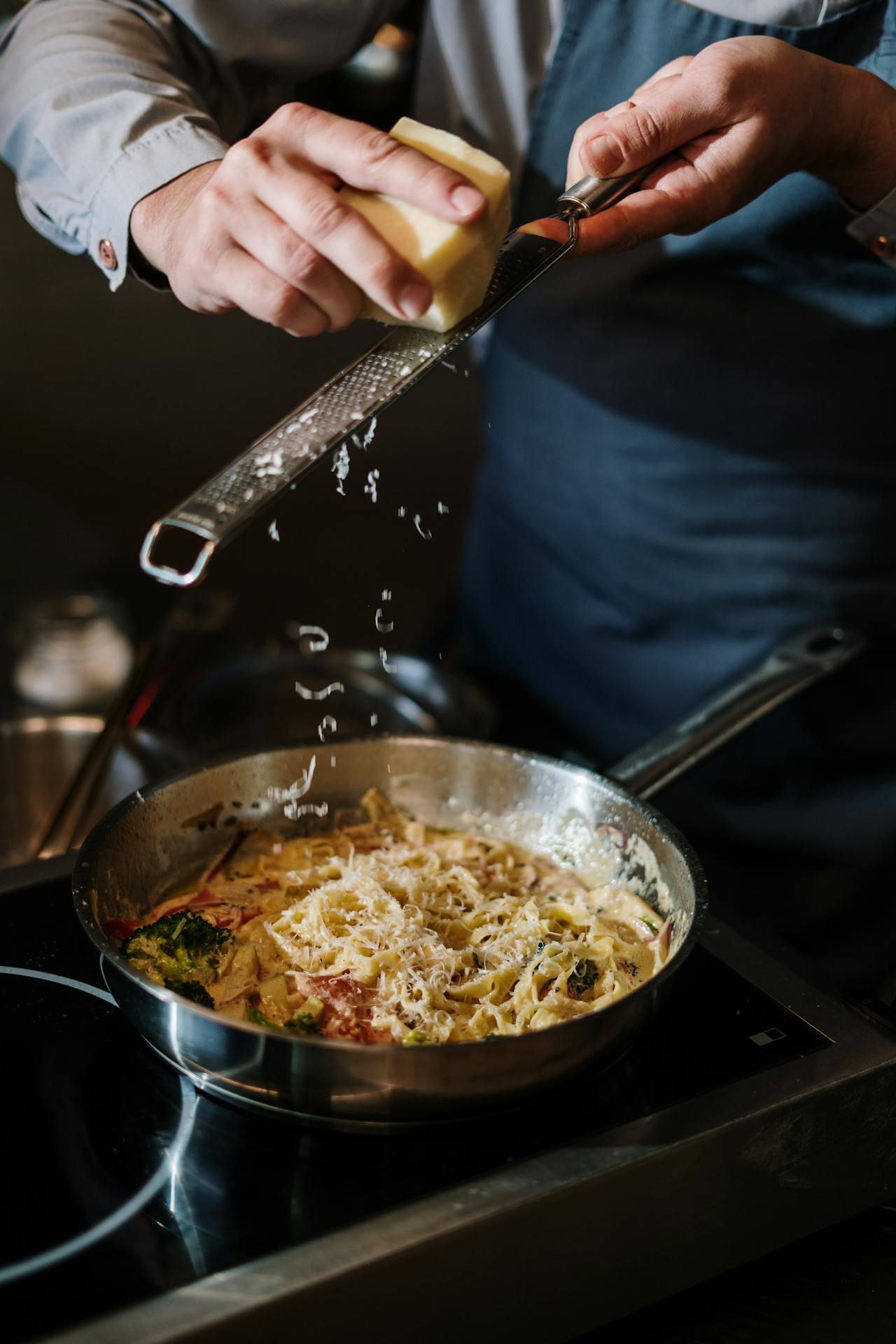 A man garnishing a pan of pasta with grated cheese | Source: Pexels