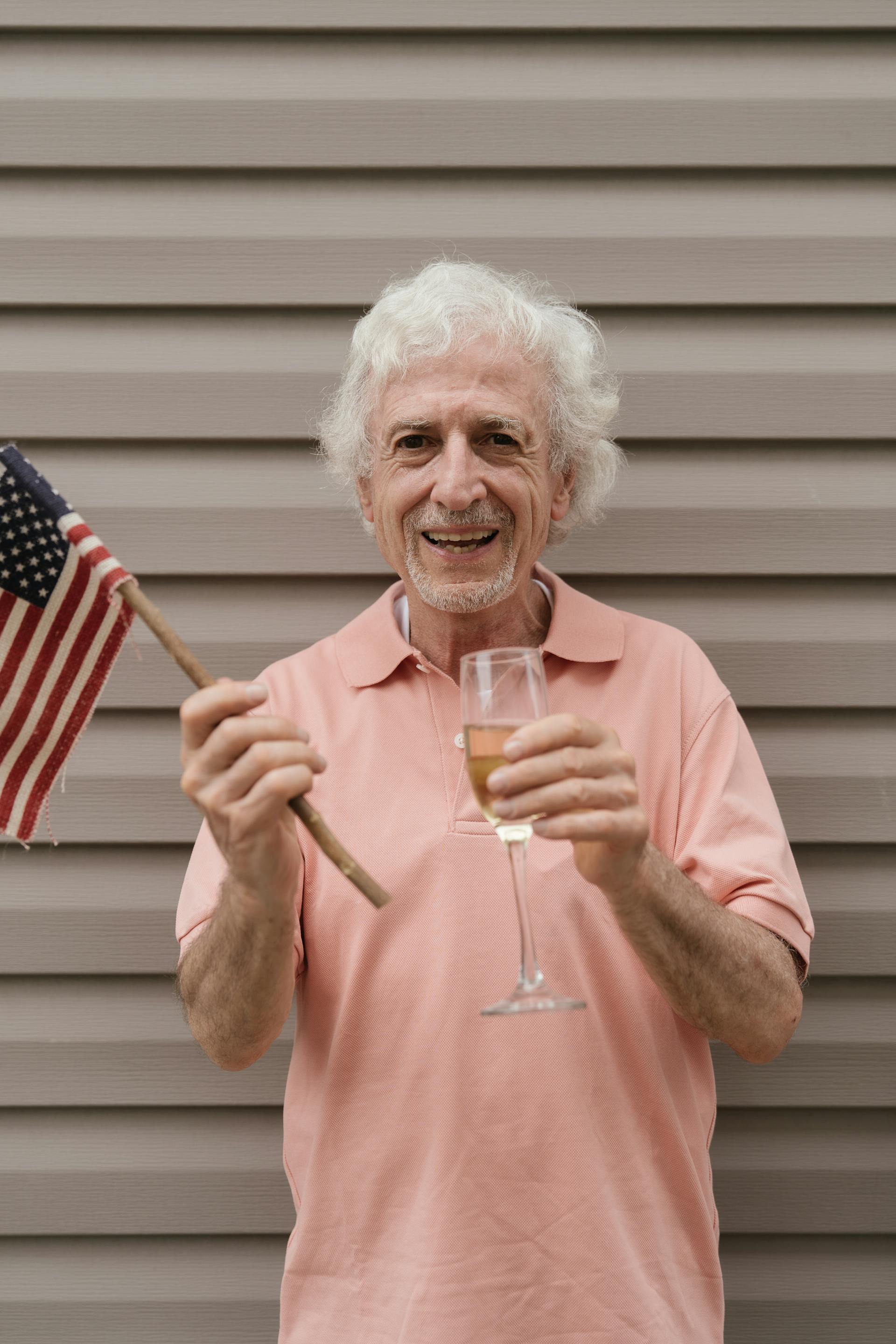 An elderly man holding the American flag and a glass of champagne | Source: Pexels