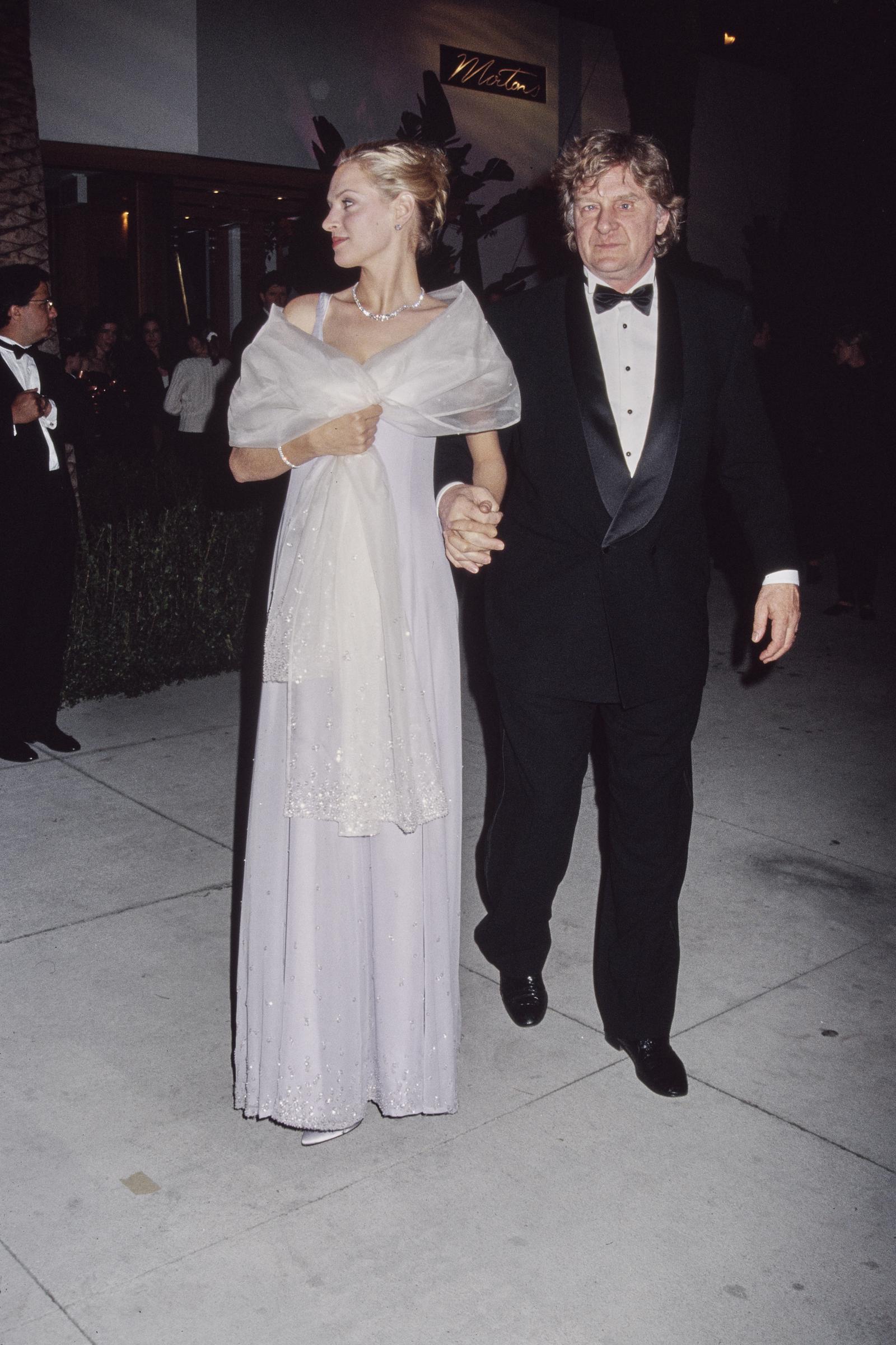 Uma Thurman, dressed in a silver gown, holds her dad Robert Thurman's hand as they attend the 1995 Vanity Fair Oscar party.