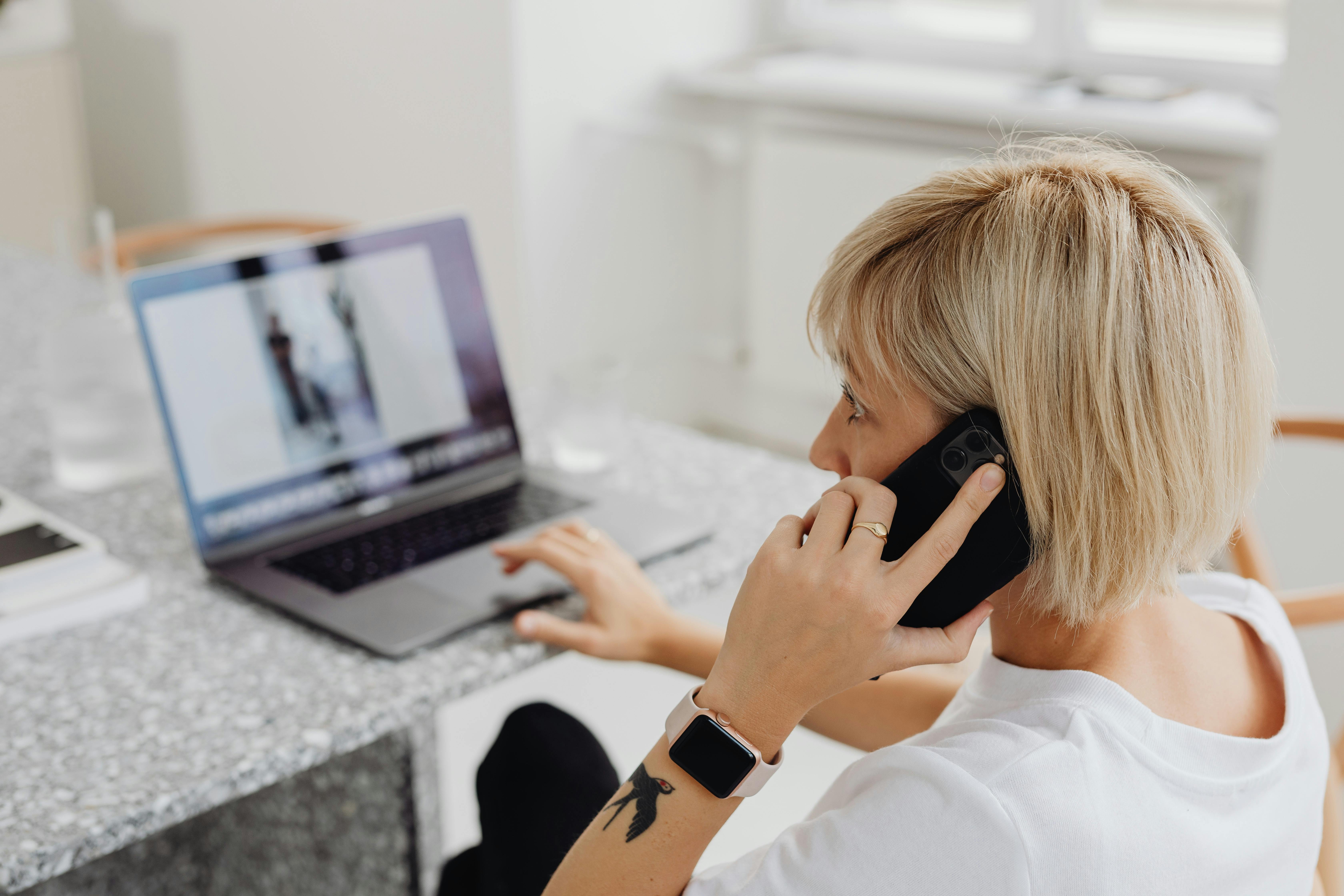 A woman using a laptop while on a phone call | Source: Pexels