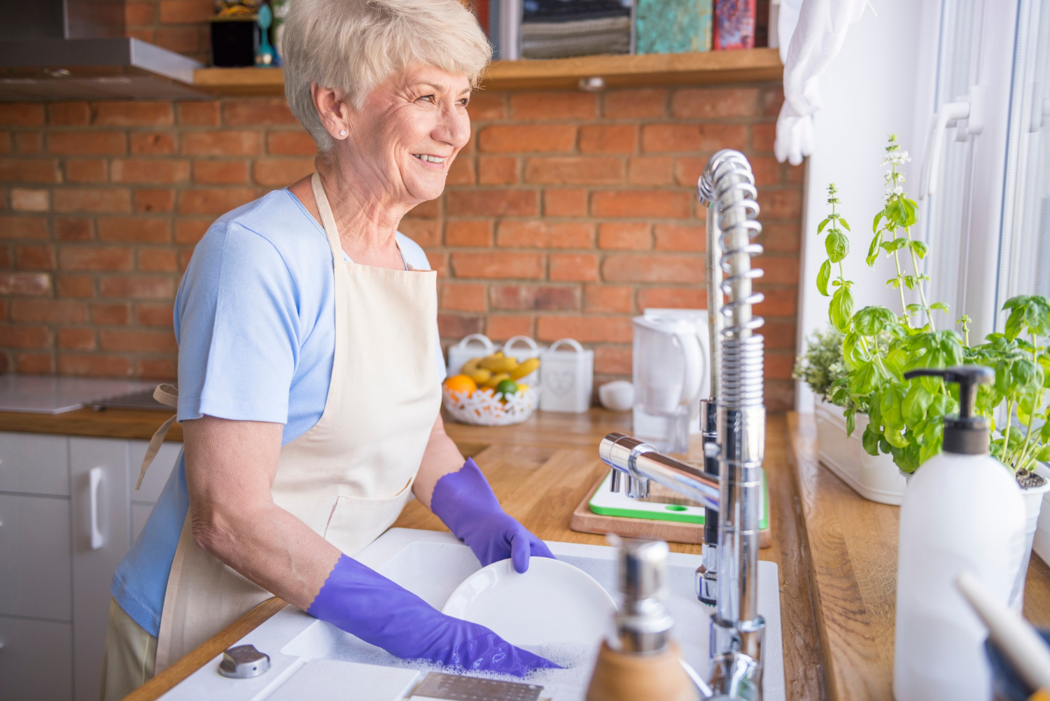 A smiling senior woman washing dishes in the kitchen | Source: Freepik