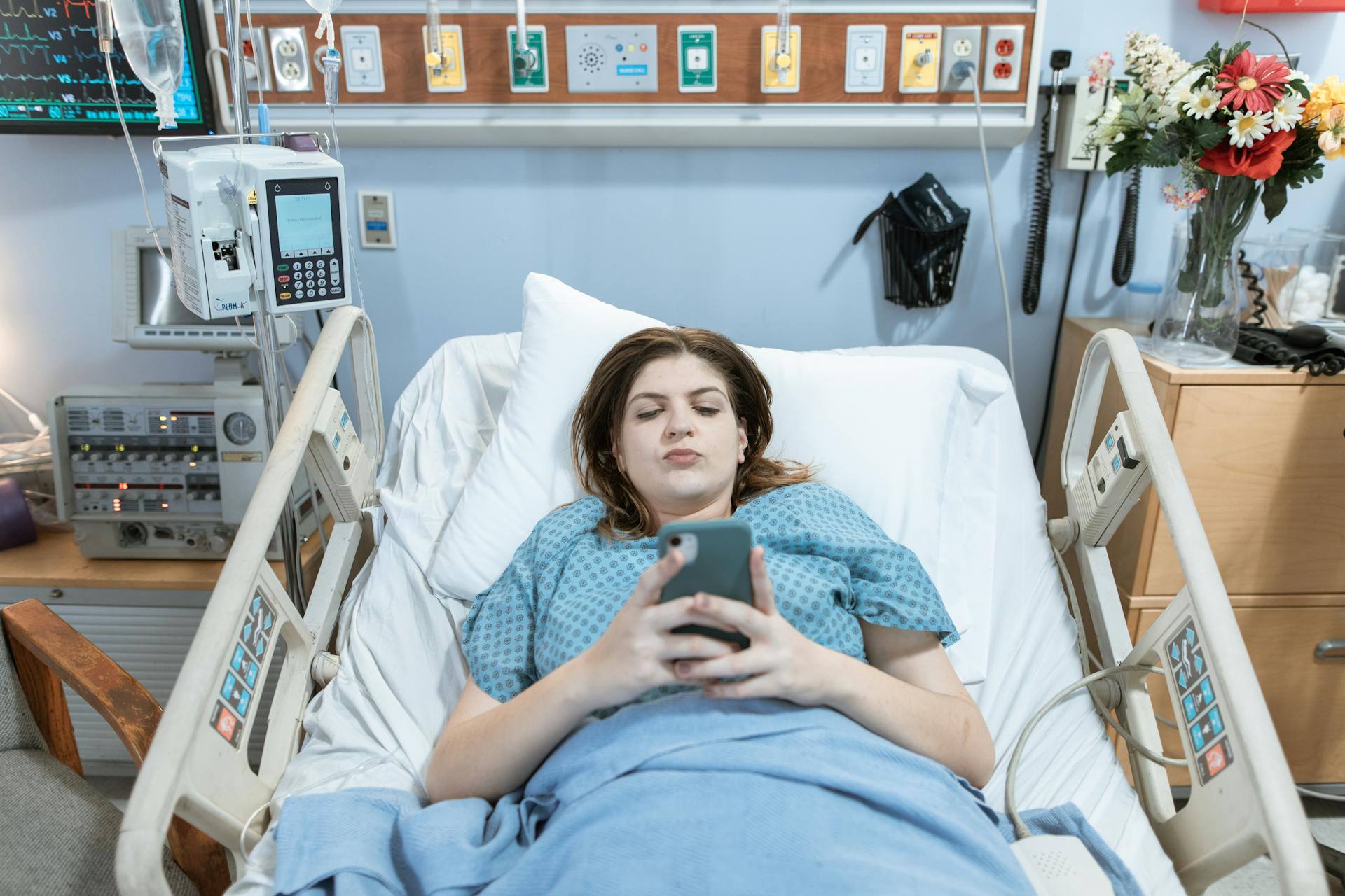 A woman looking at her phone while lying in a hospital bed | Source: Pexels