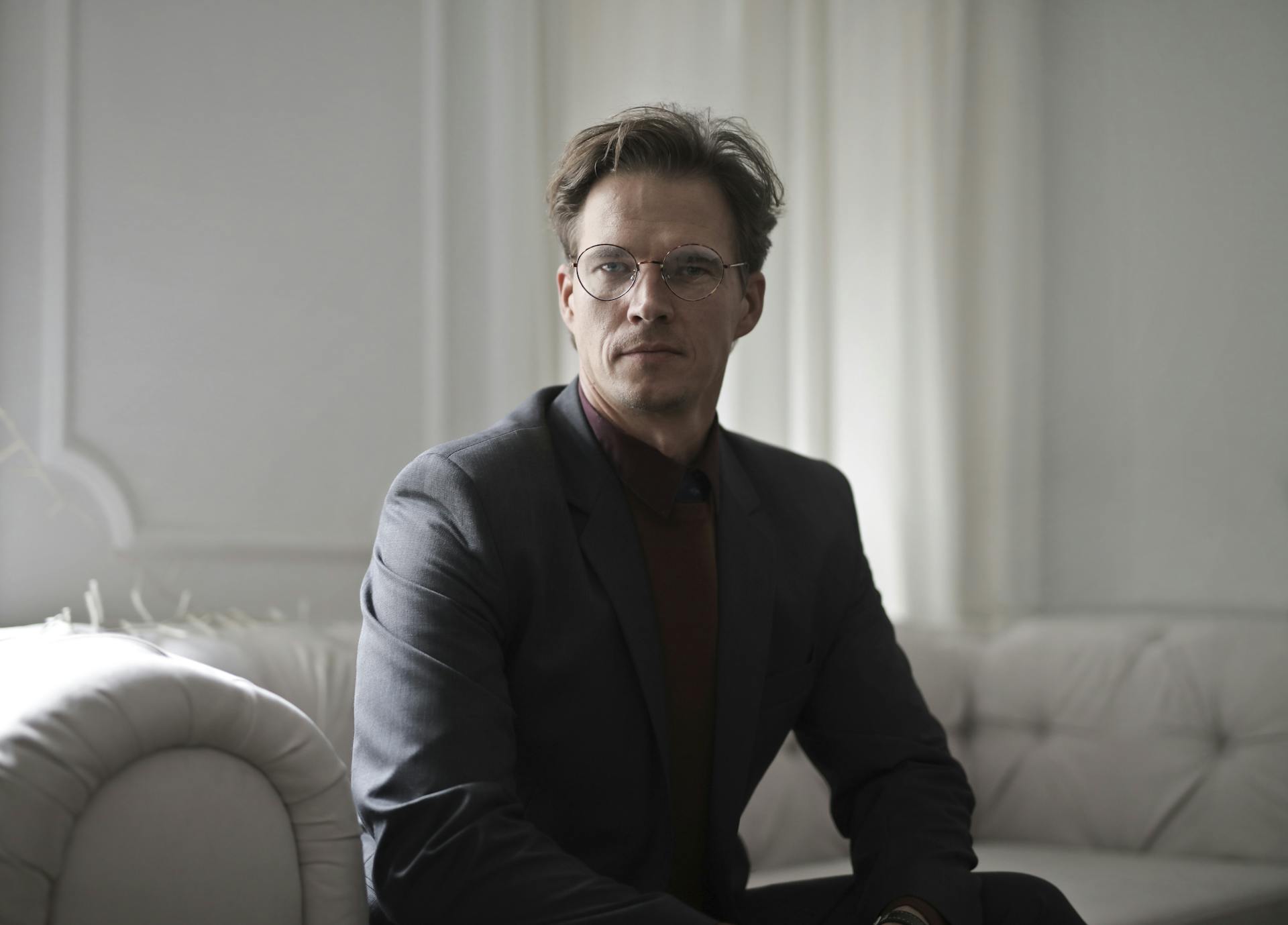 A man wearing a blazer and eyeglasses sitting on a sofa | Source: Pexels