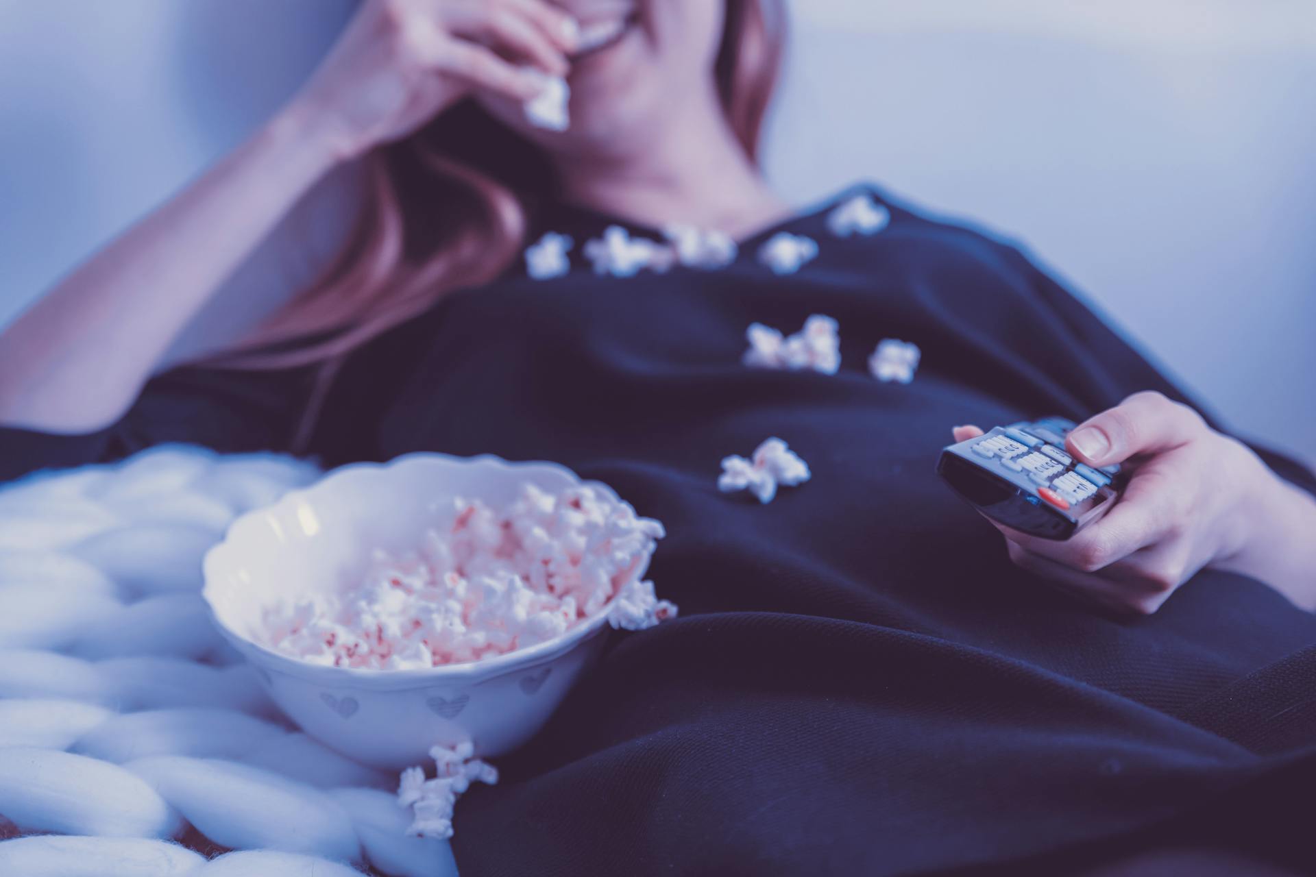 A woman eating popcorn while holding a TV remote | Source: Pexels