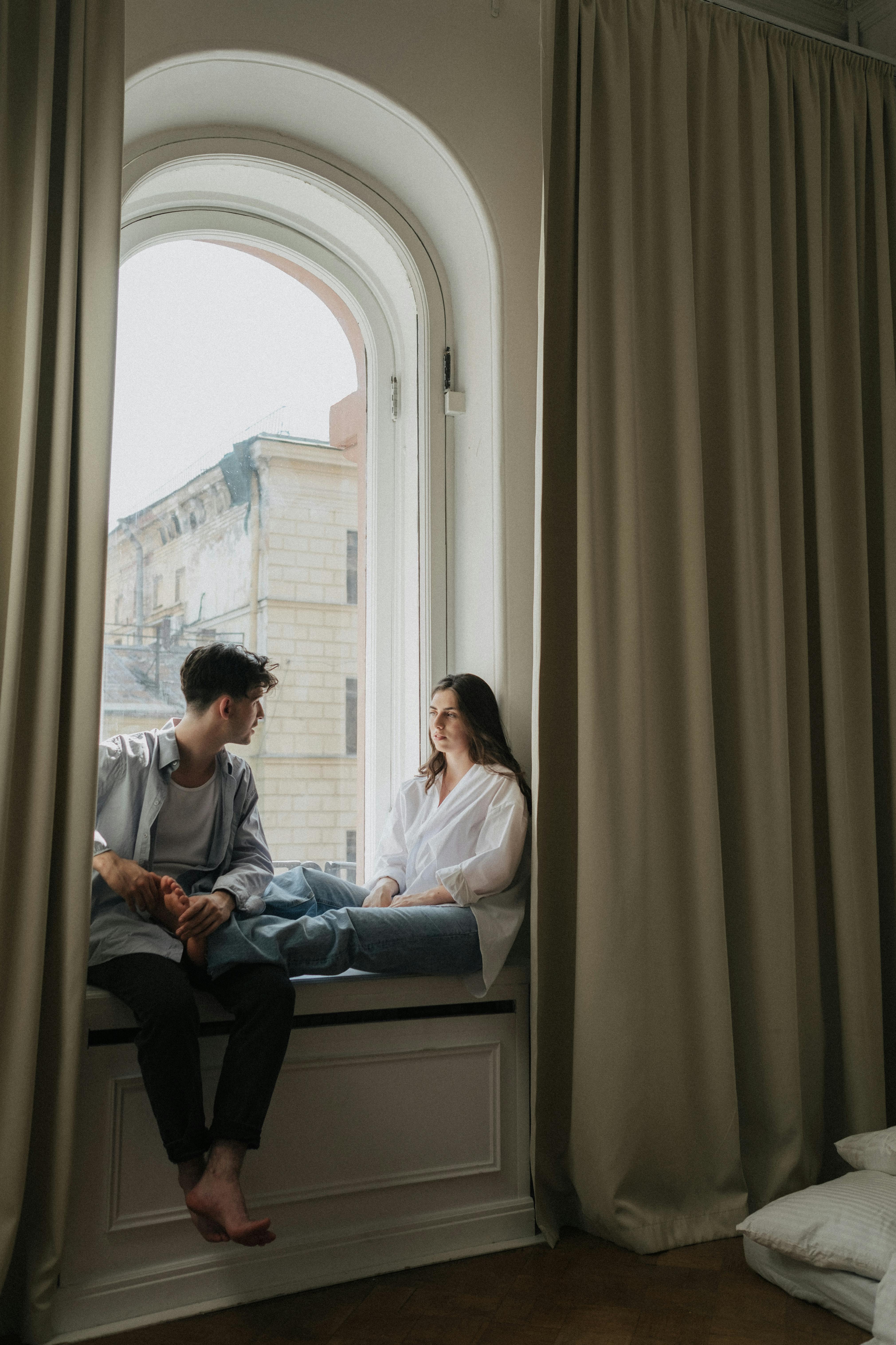 Man and woman sitting on the window talking | Source: Pexels