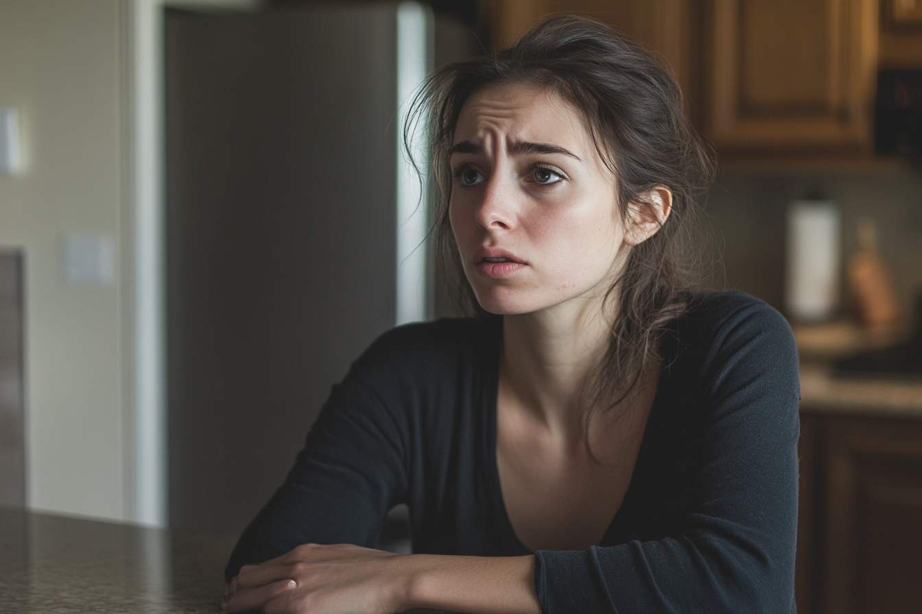 A sad and shocked woman seated at kitchen table | Source: Midjourney