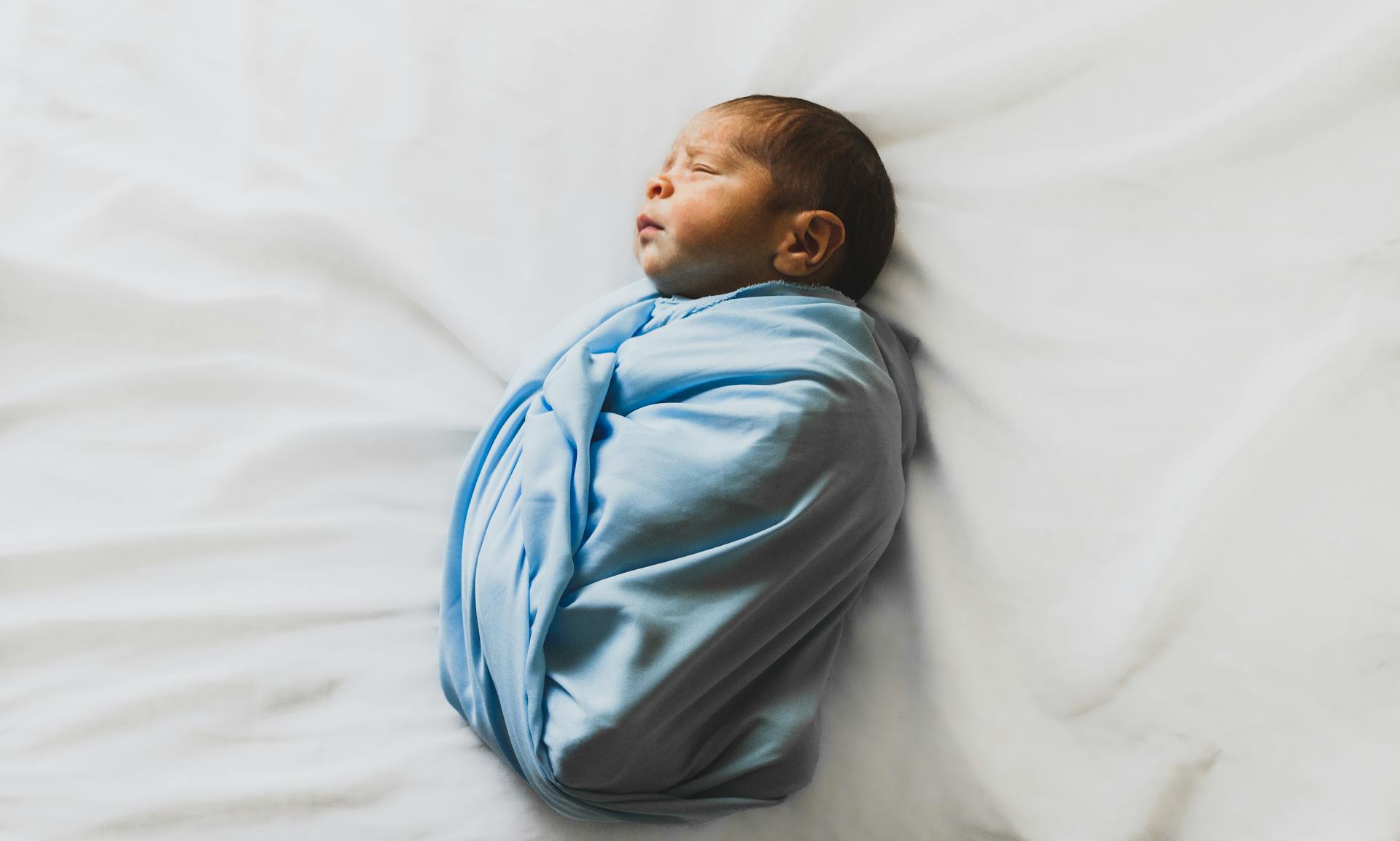 An adorable newborn baby covered in a blue blanket | Source: Pexels