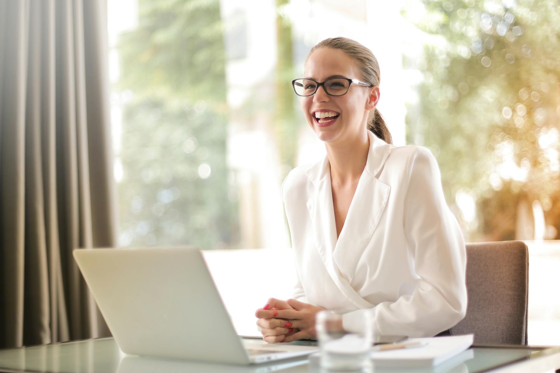 A woman laughing while working on her laptop in the office | Source: Pexels