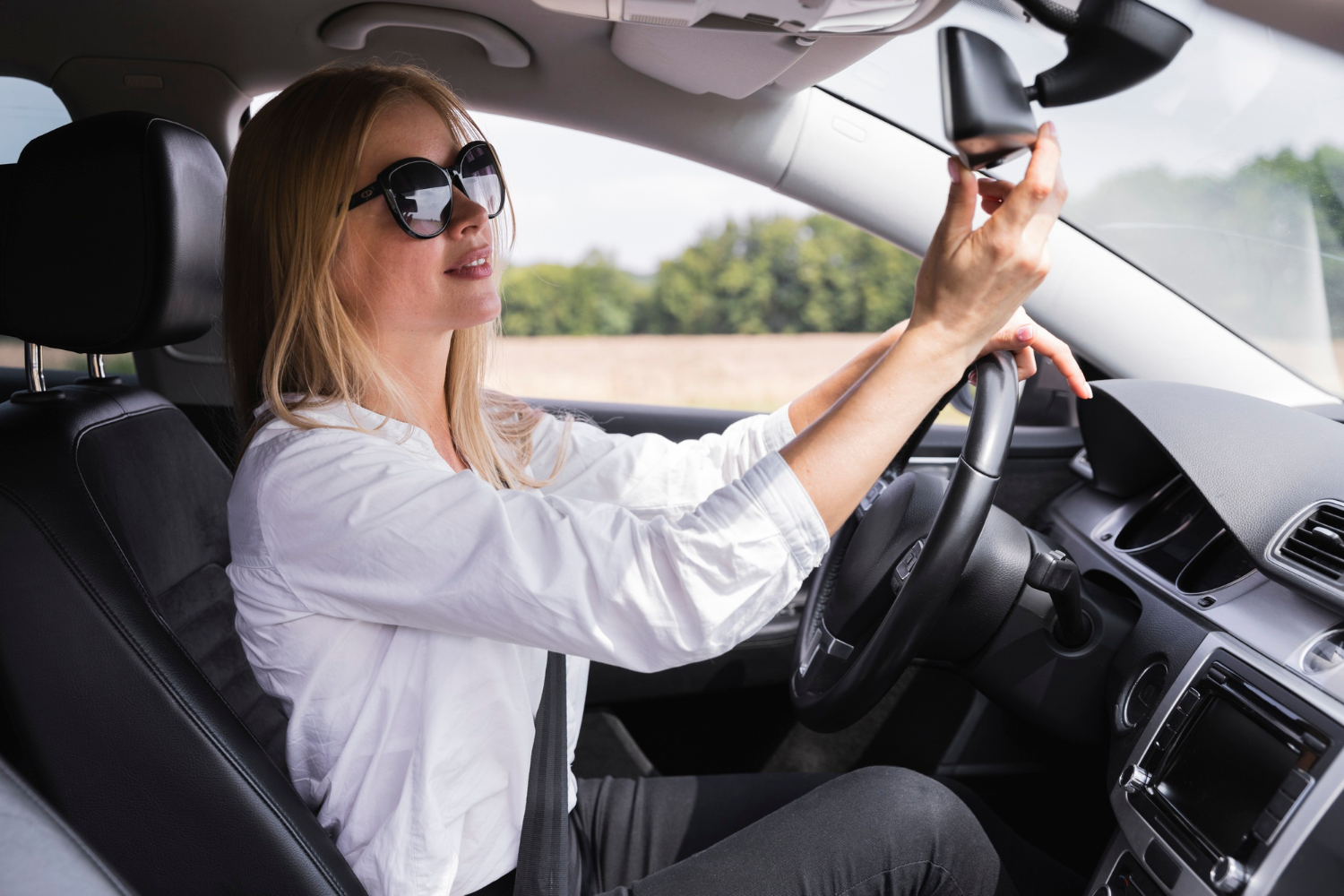 A woman driving her car while adjusting the rearview mirror | Source: Freepik