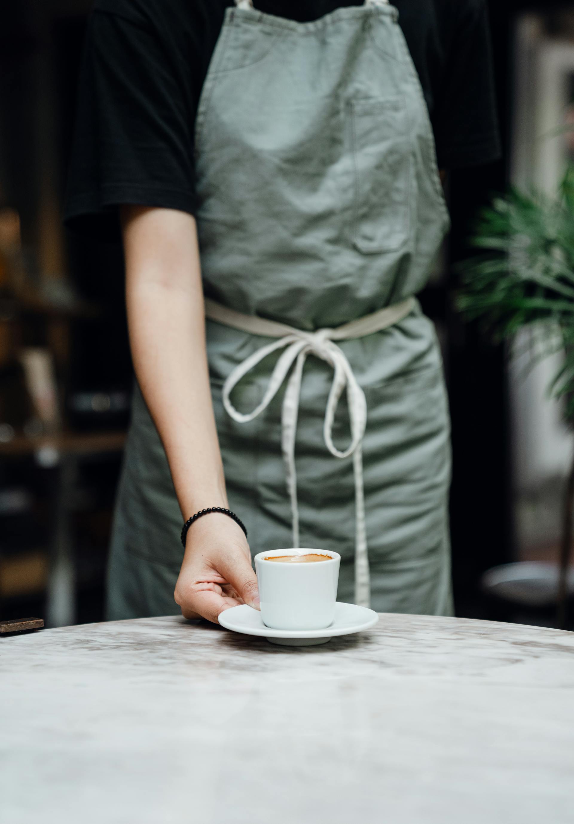 Cropped shot of a waitress placing a cup of coffee on a table | Source: Pexels