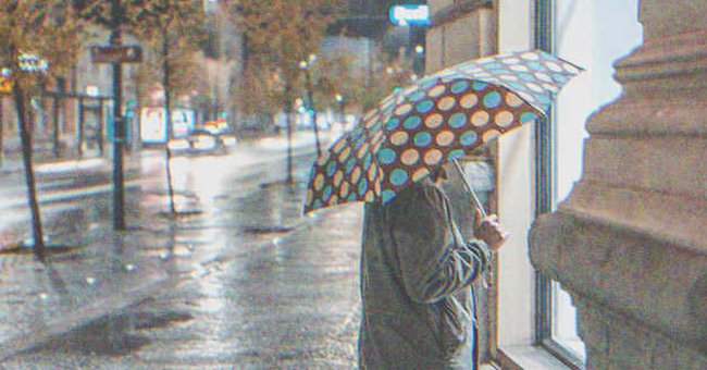 An old lady holding an umbrella and looking inside a business | Source: Shutterstock