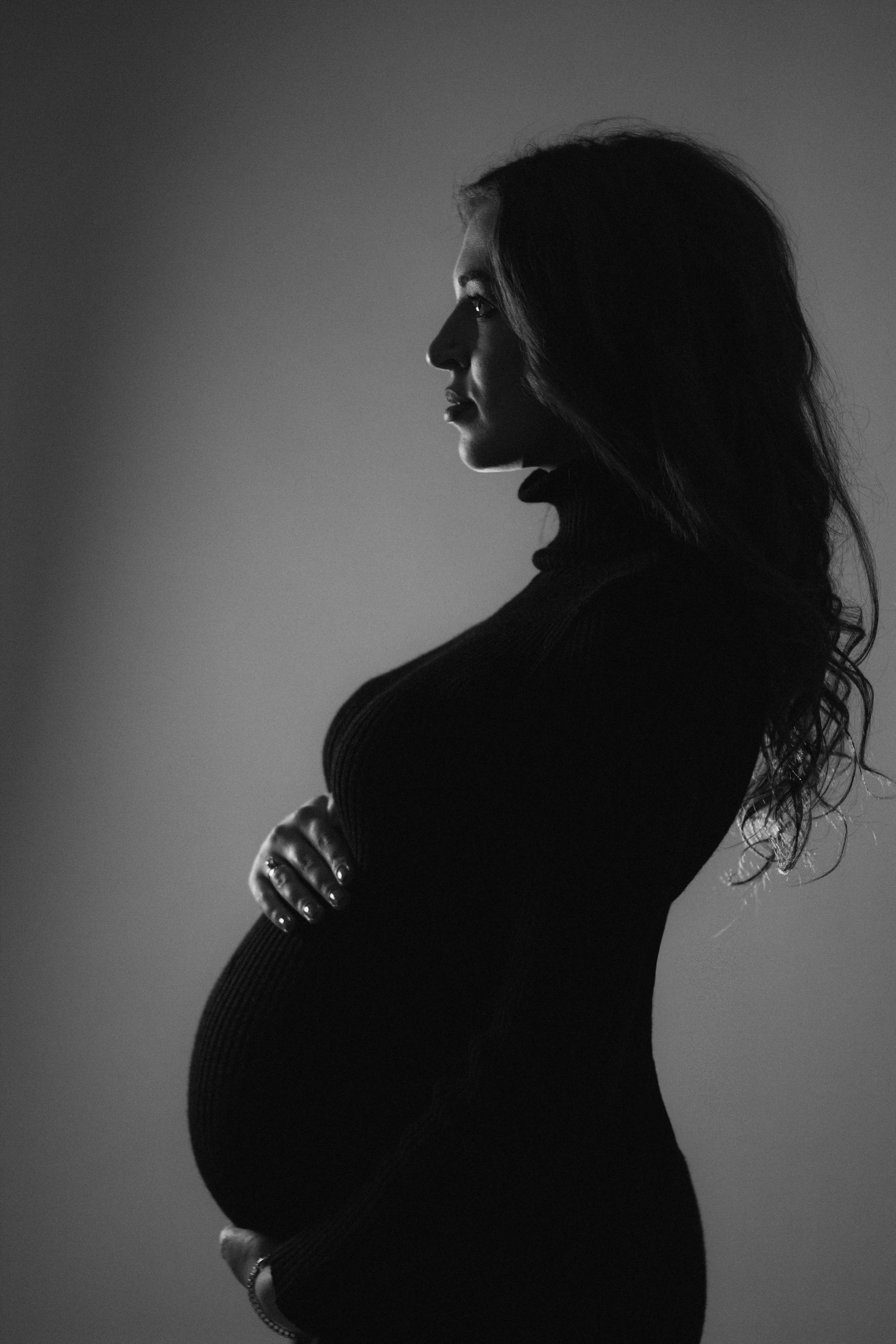 A black and white side-profile image of a pregnant woman holding her baby bump | Source: Pexels