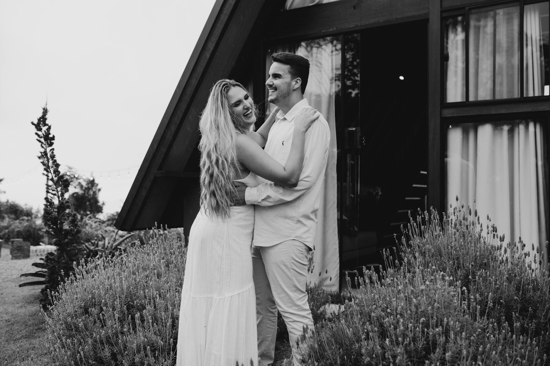A smiling couple hugging while standing in front of a modern A-frame cabin | Source: Pexels