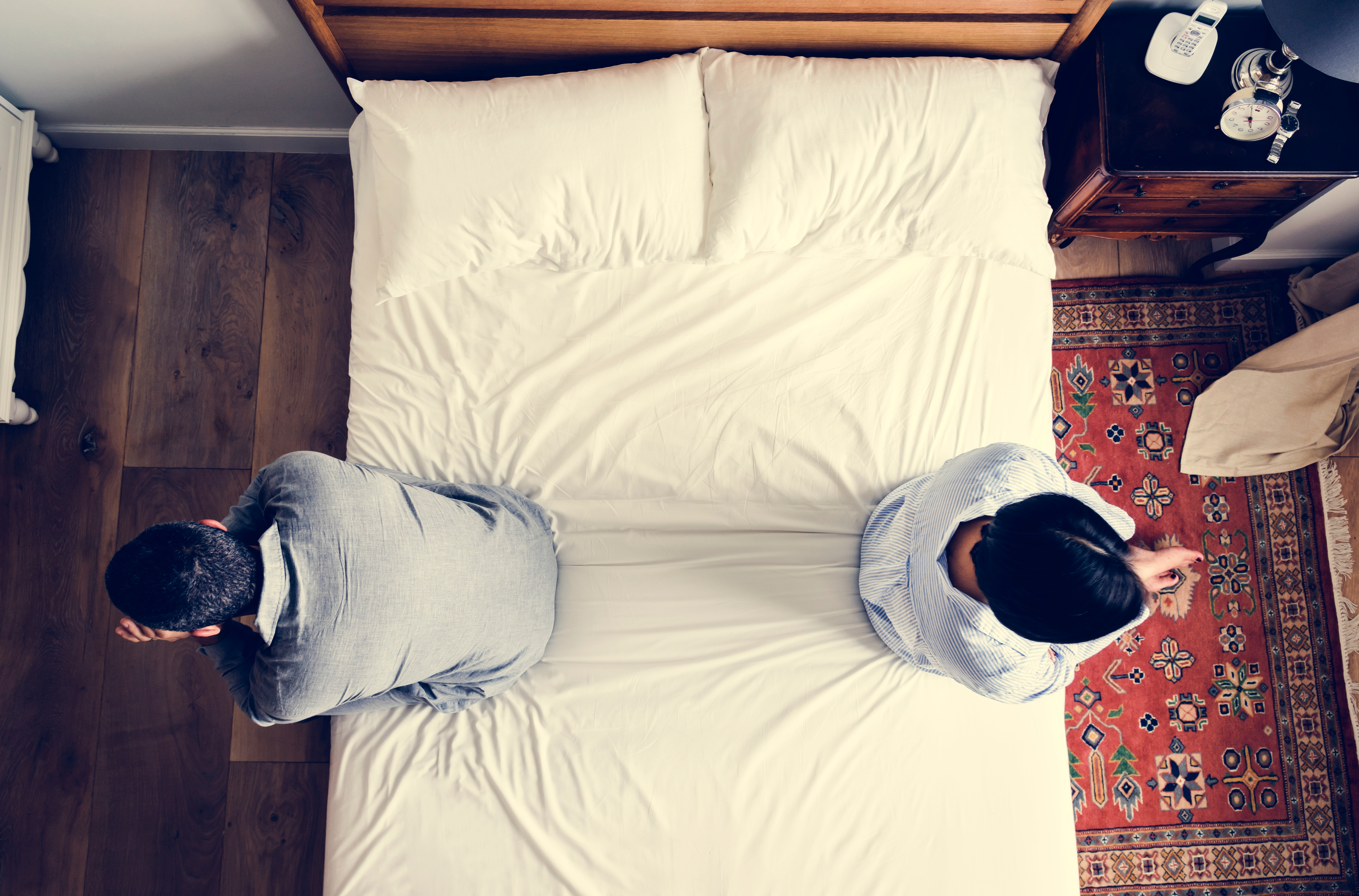 A couple sitting with their backs to each other on a bed | Source: Shutterstock