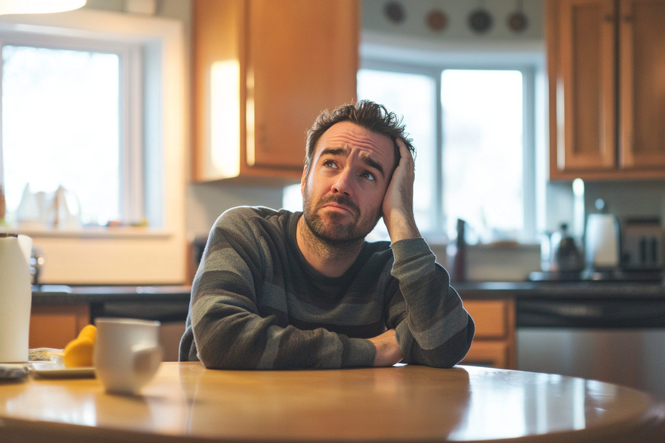 Un homme assis dans une cuisine, l'air confus | Source : Midjourney