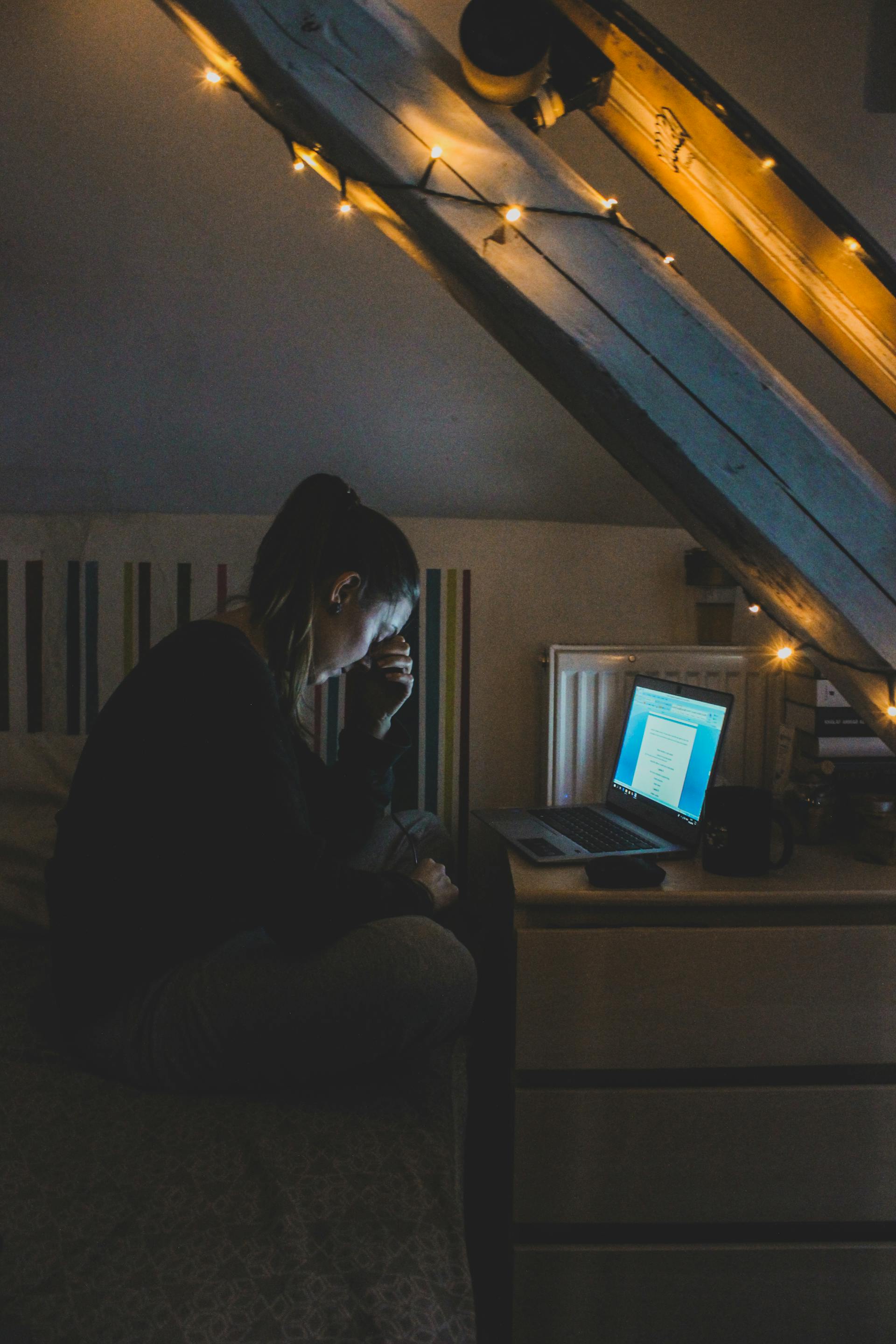 A distant shot of a woman looking distraught while using her laptop at night | Source: Pexels