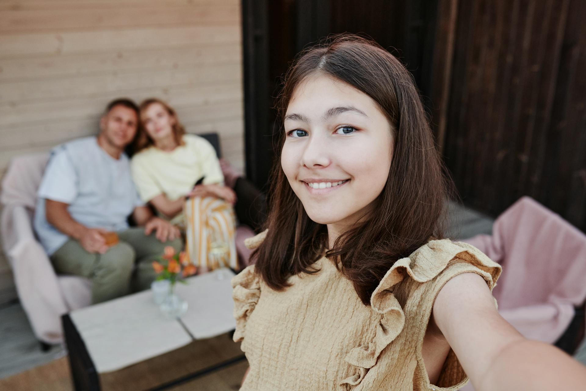 A teen girl taking a selfie with two adults in the background | Source: Pexels