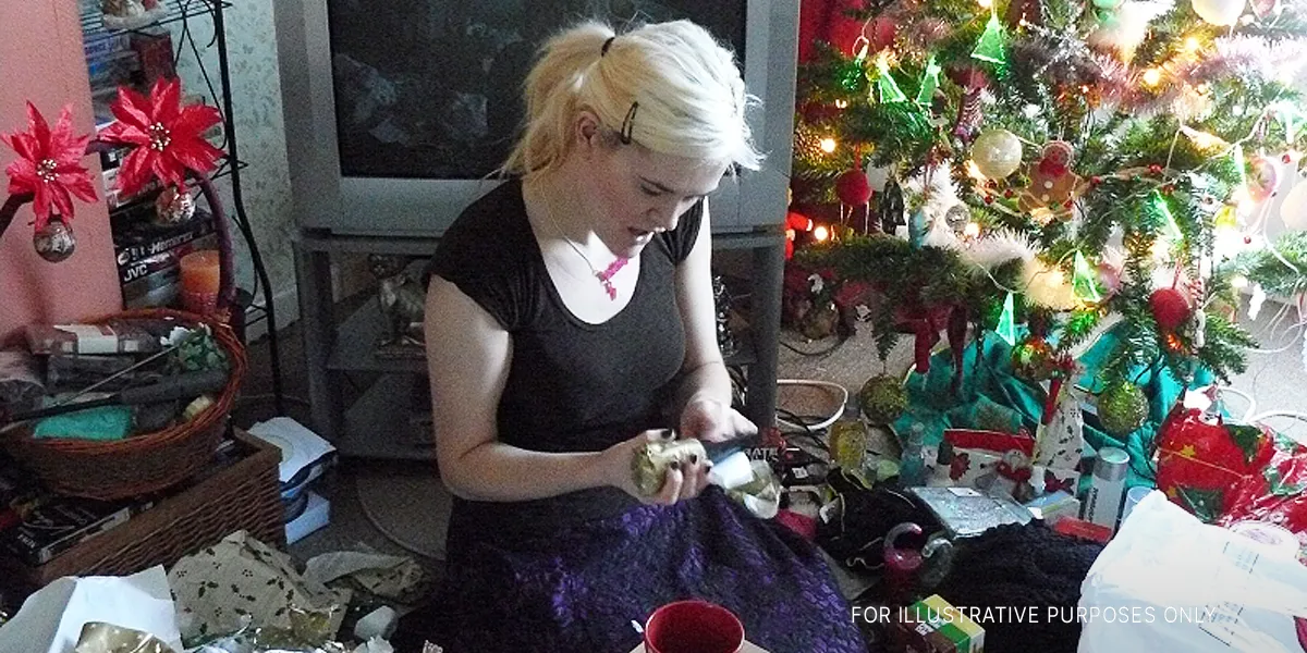 A young woman unwraps a Christmas present | Source: Flickr