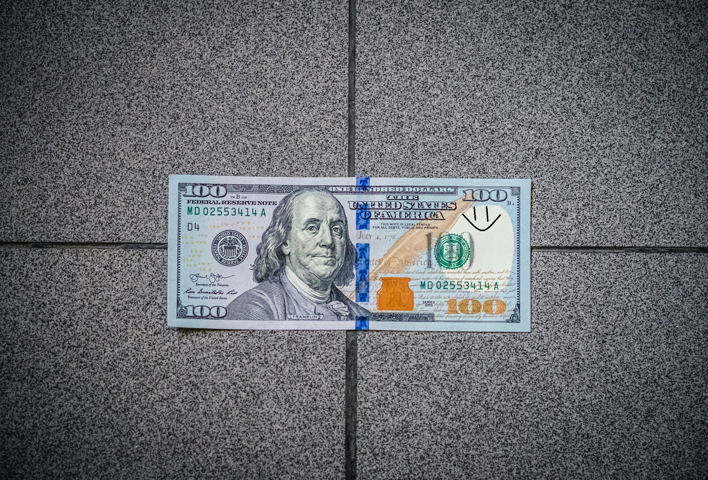 A $100 bill on the floor with a smiley face drawn on it | Source: Unsplash