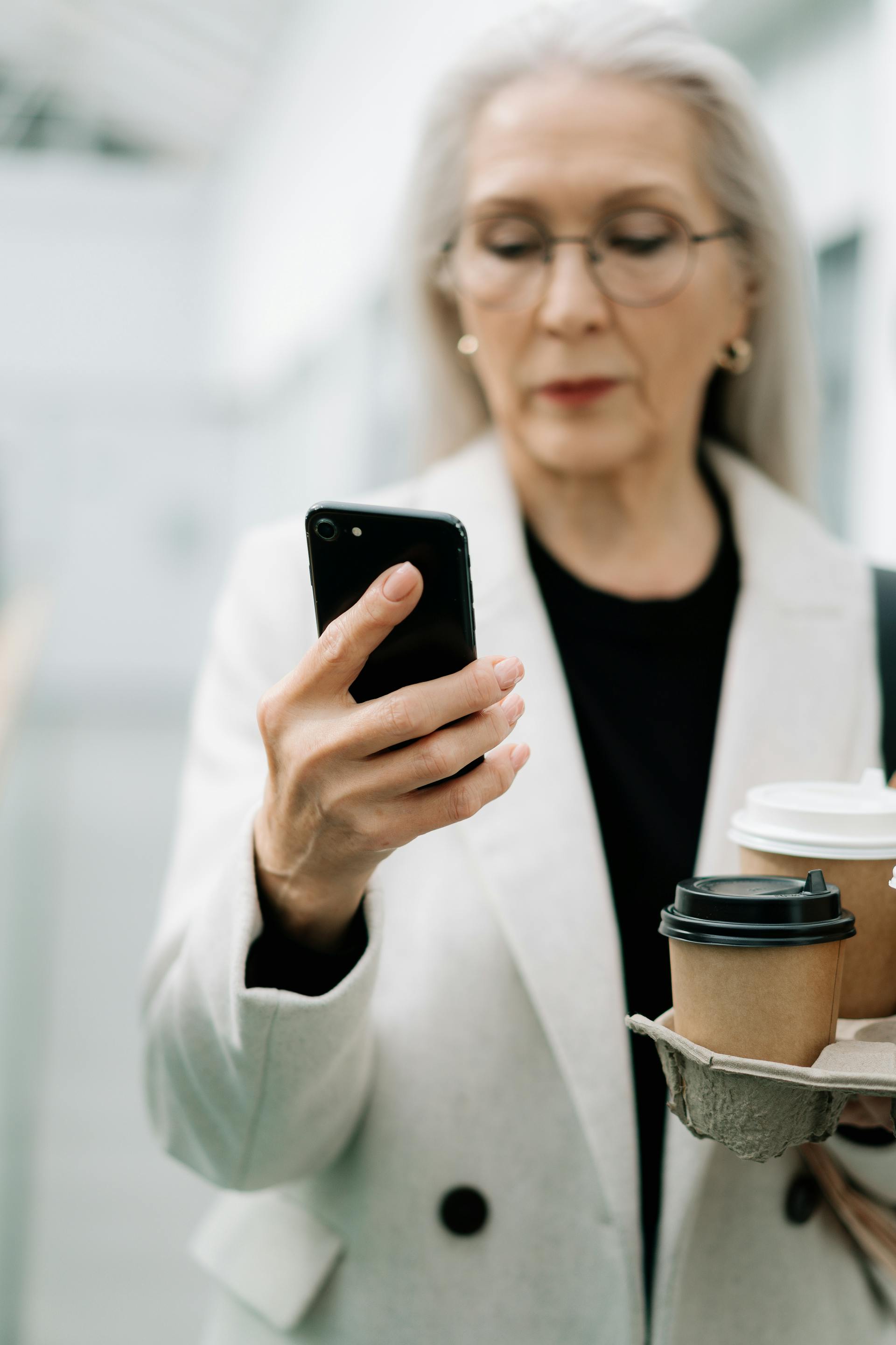 An elderly woman using her phone while holding coffee | Source: Pexels