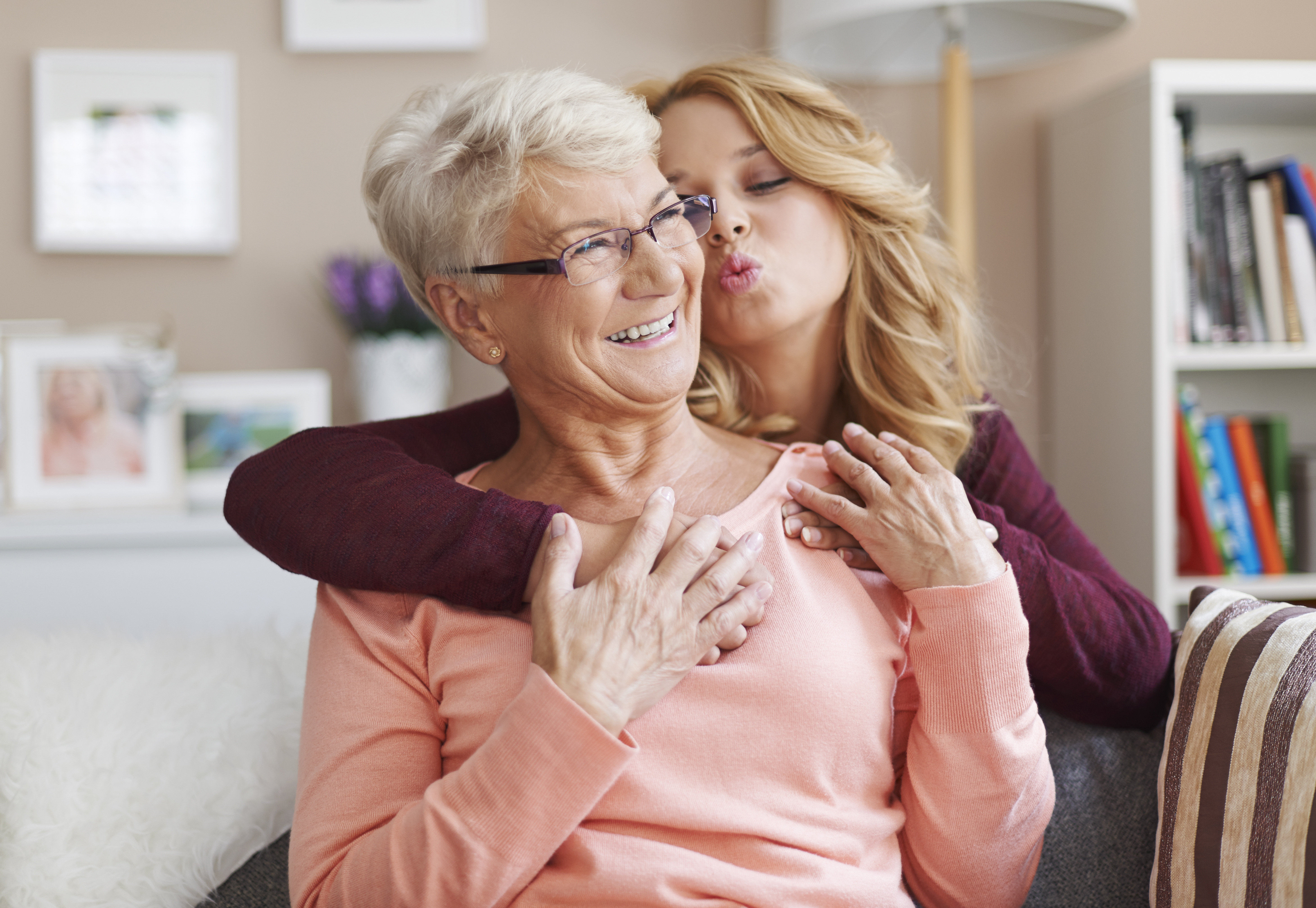 A teen girl hugging her smiling grandmother from behind and attempting to kiss her | Source: Freepik